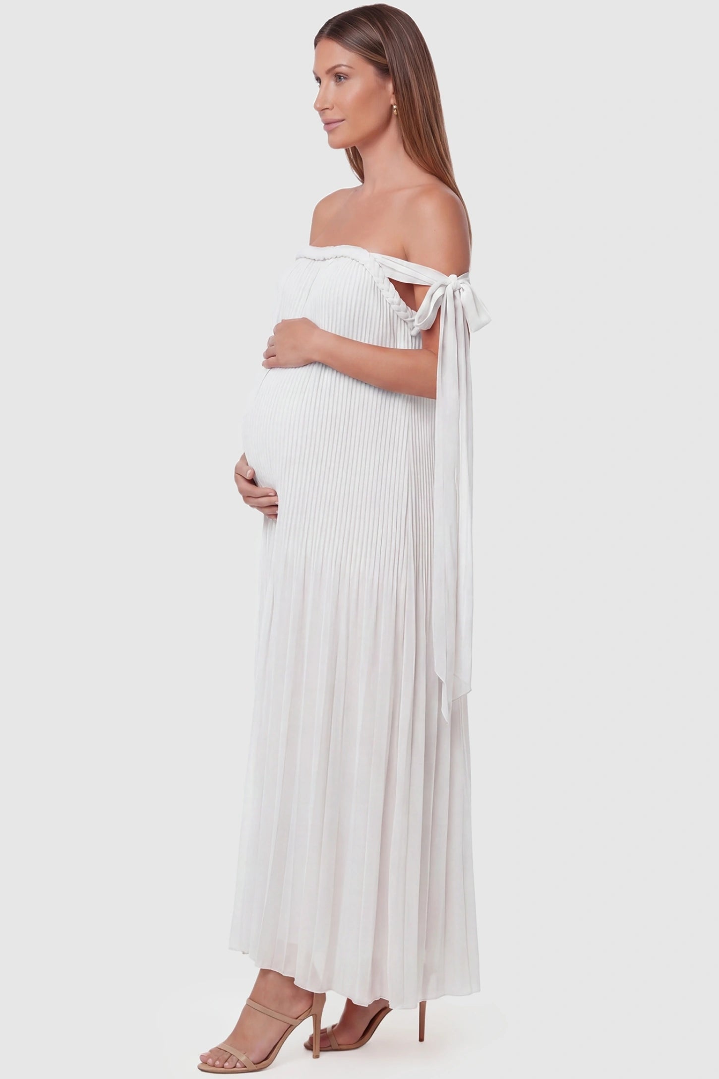 Pleated Braided Cold-Shoulder Maxi Maternity Gown Pleated Braided Cold-Shoulder Maxi Maternity Gown in White featuring flowing pleated chiffon on a pregnant model, side view.