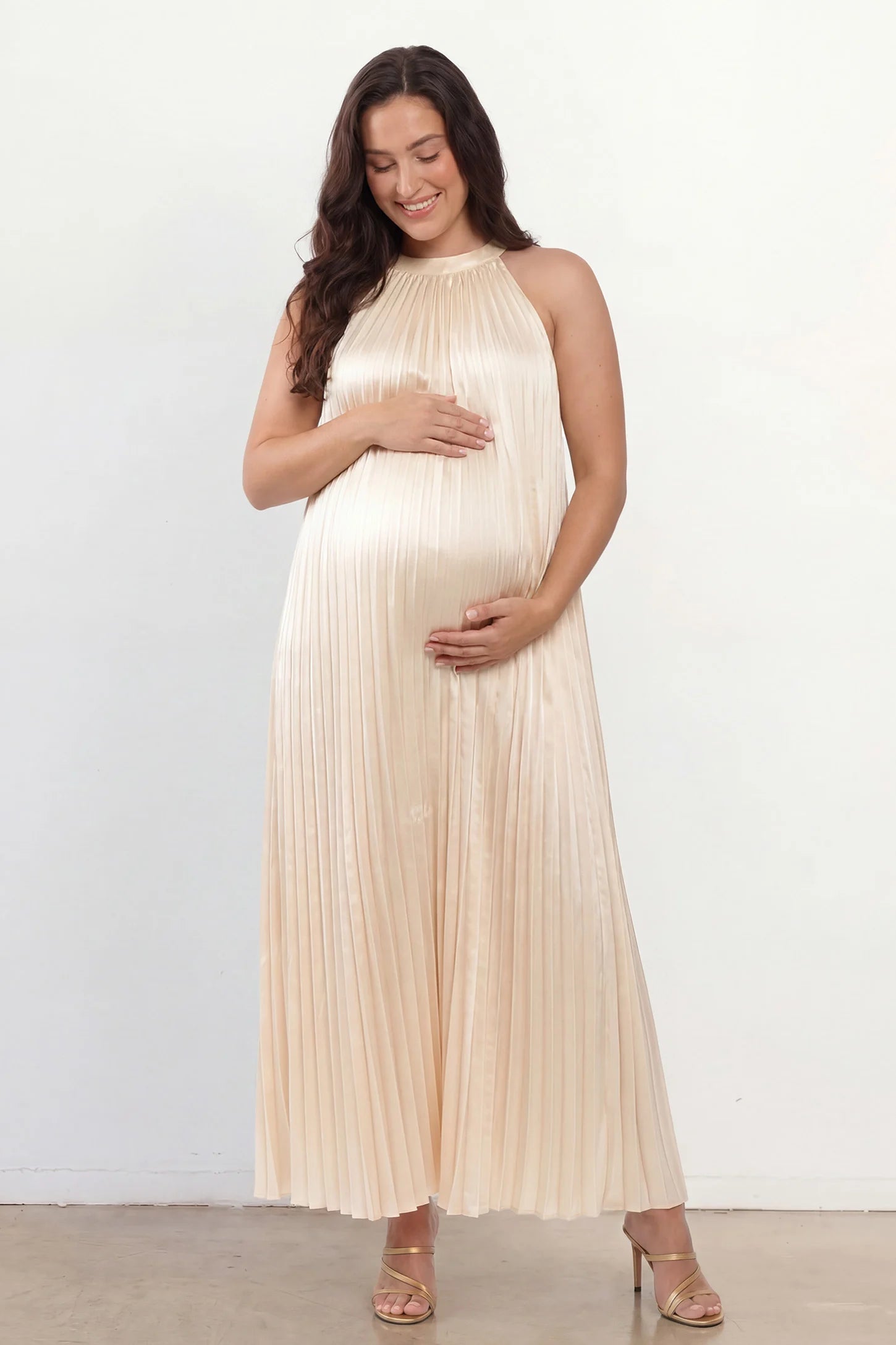 Pleated Faux Silk Halter Maternity Maxi Dress Pleated Faux Silk Halter Maternity Maxi Dress in Champagne featuring micro-pleat texture on a plus size postpartum model facing front.