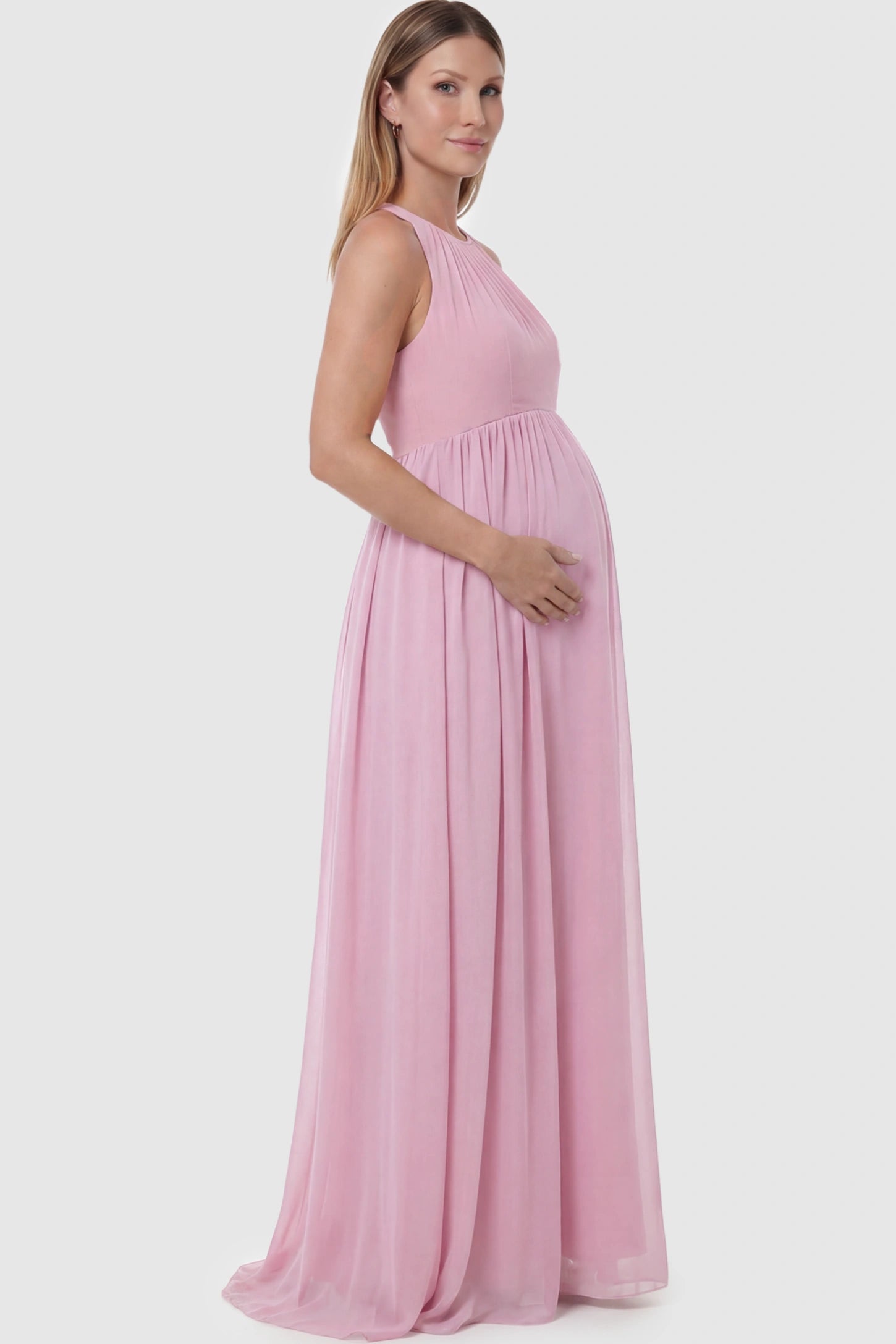 Pleated Mesh Sleeveless Maternity Photoshoot Dress Pleated Mesh Sleeveless Maternity Maxi Dress in pink featuring an empire waist on a pregnant model showing side.