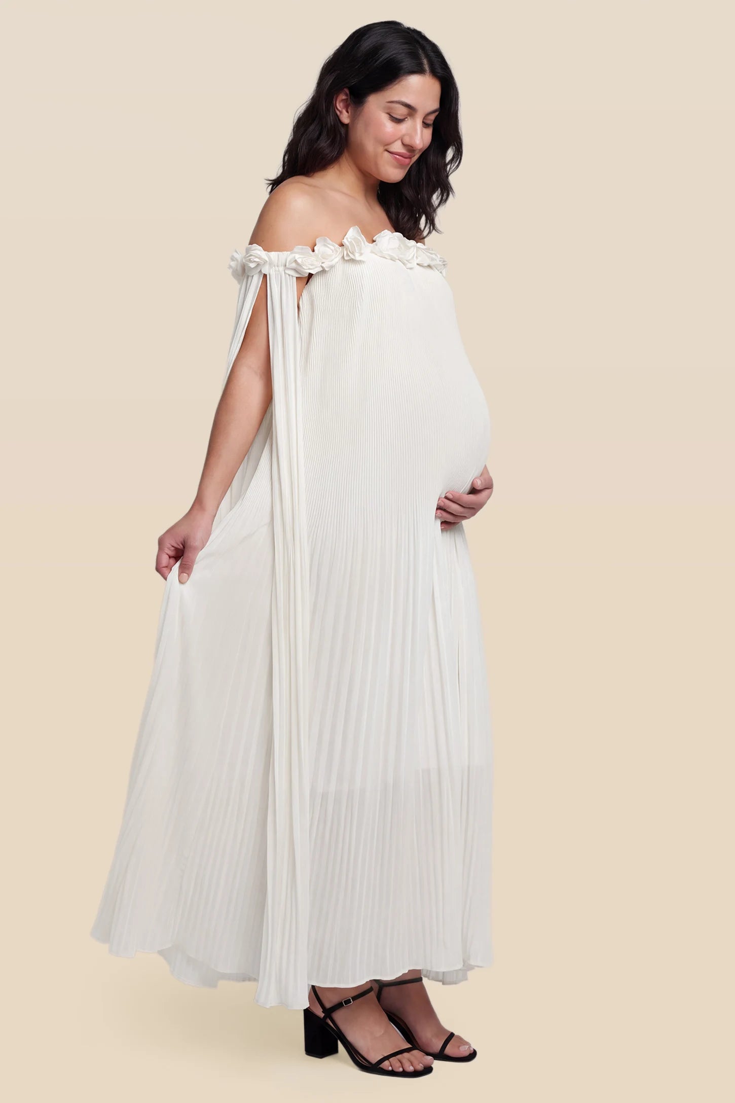 Pleated Off-Shoulder Maternity Gown with Rosettes Pleated Off-Shoulder Maternity Gown with Rosettes in White with flowy pleated skirt, side view on a pregnant model.