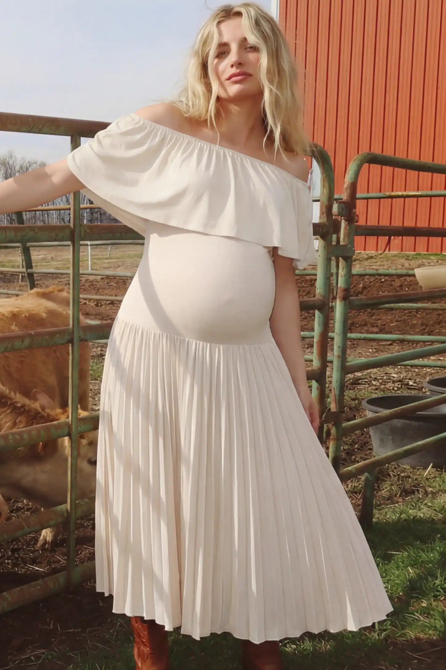 Pleated Off Shoulder Maternity Maxi Dress  in Beige featuring high stretch pleated maxi skirt on a pregnant model during outdoor photoshoot front view.