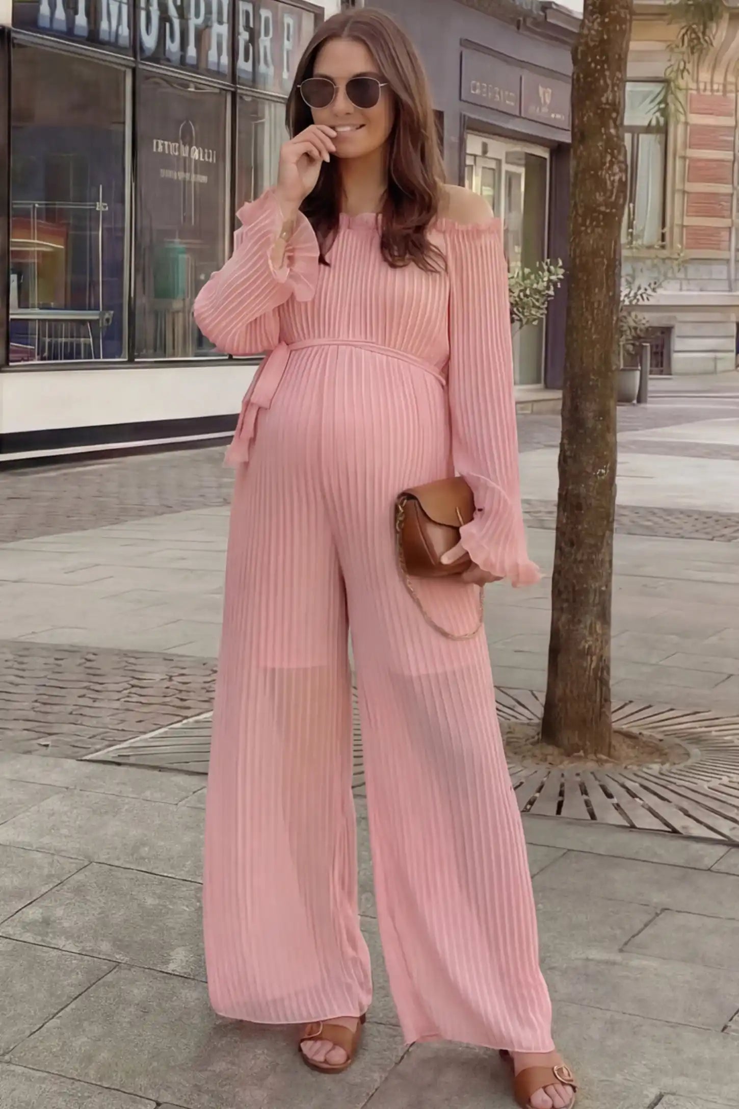 Pleated Off Shoulder Tie-Waist Maternity Jumpsuit Pleated Off Shoulder Tie-Waist Maternity Jumpsuit in Pink featuring a wide-leg silhouette on a pregnant woman in outdoor setting, front view.