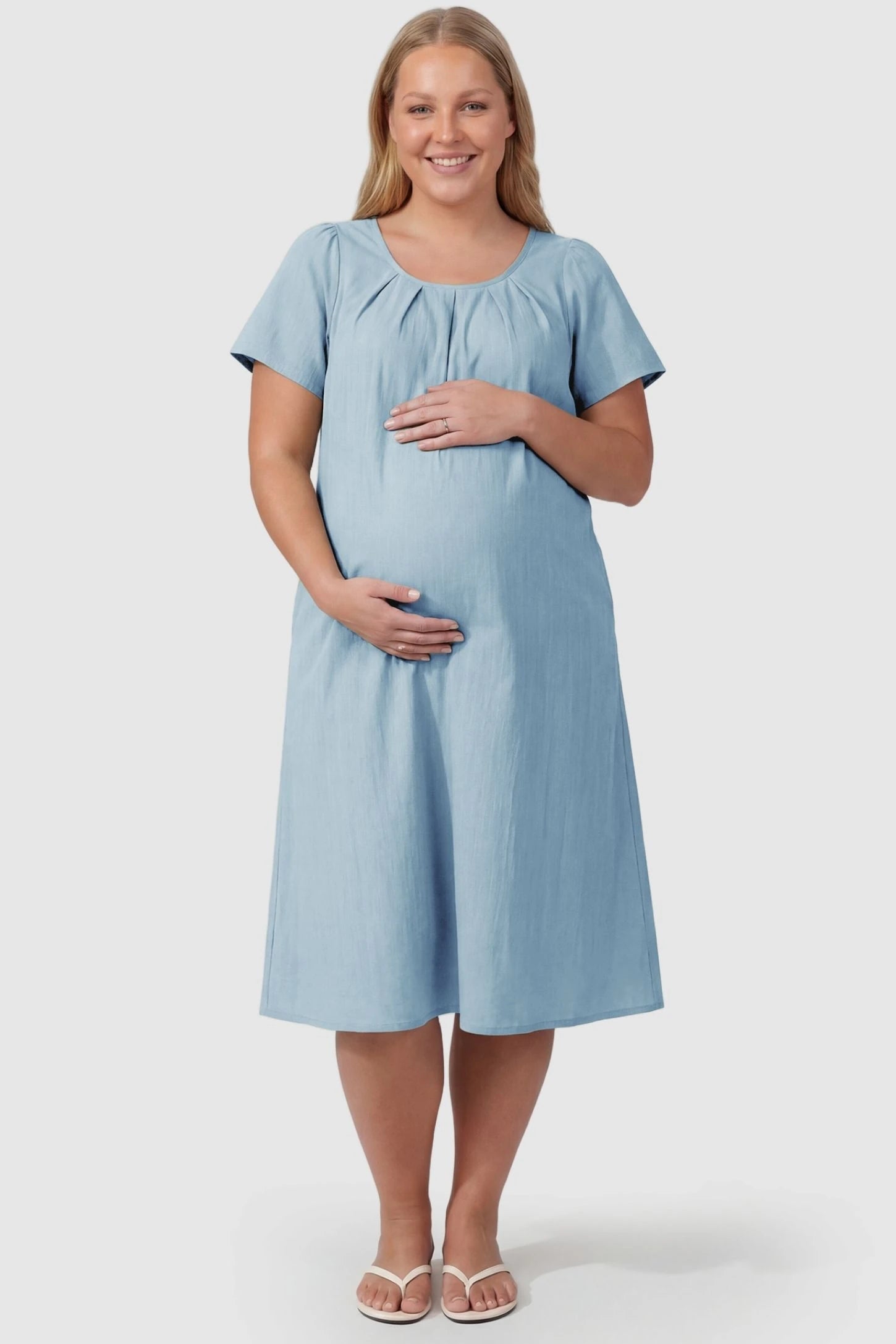Pleated Round Neck Flowy Midi Maternity Dress Pleated Round Neck Flowy Midi Maternity Dress in Blue featuring stretchy fabric on a plus size pregnant model, front view.