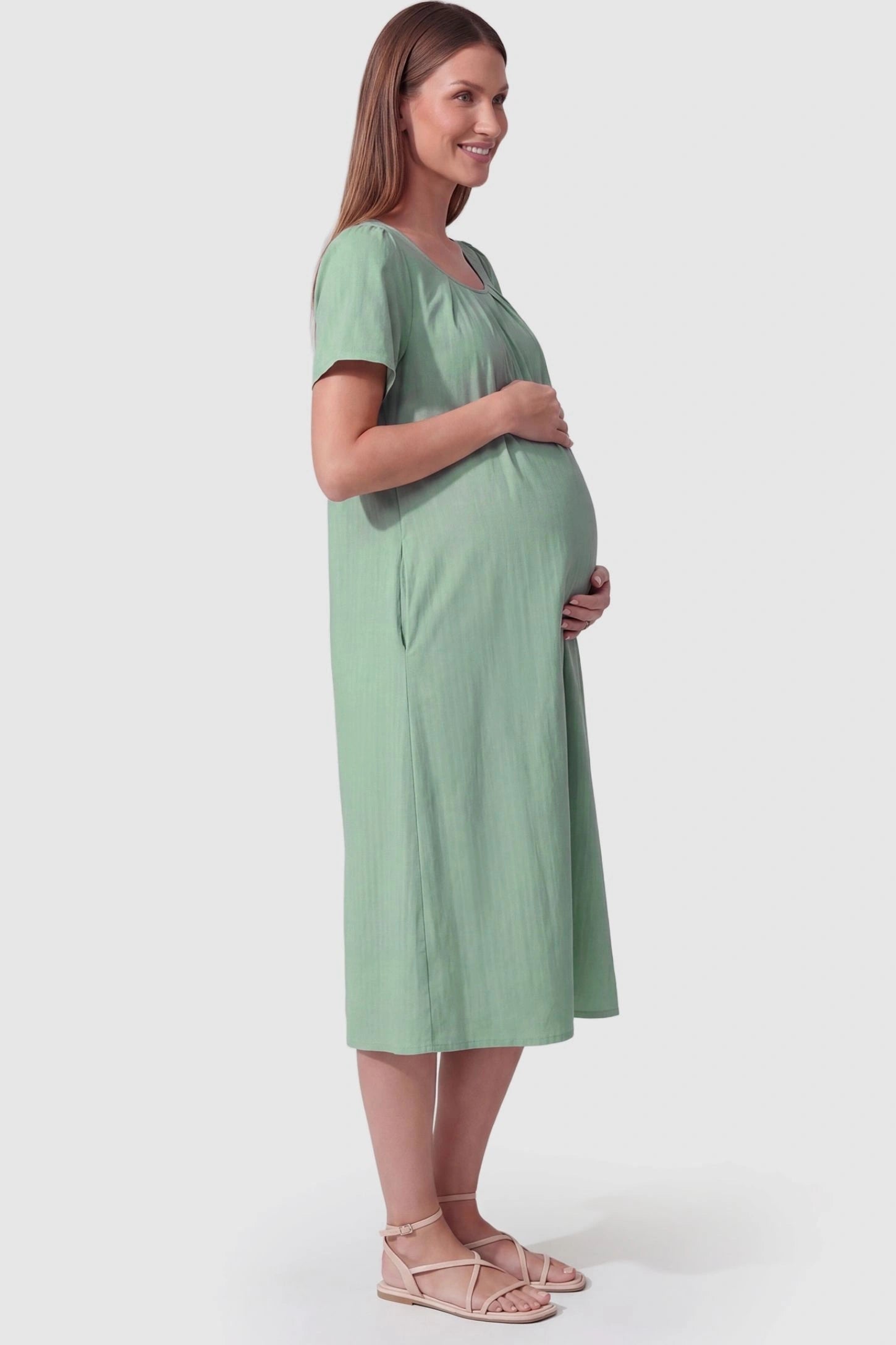 Pleated Round Neck Flowy Midi Maternity Dress Pleated Round Neck Flowy Midi Maternity Dress in Lake Blue featuring a flowy silhouette on a pregnant model, side view.
