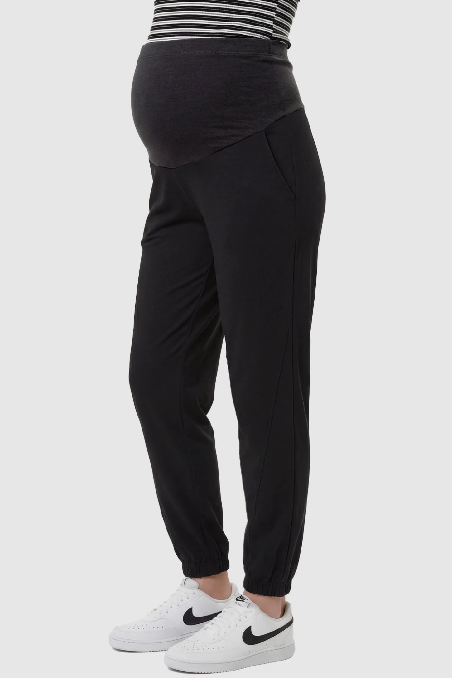 Full Panel Pocketed Maternity Jogger Pants Full Panel Pocketed Maternity Jogger Pants in Black featuring a jersey belly panel on a pregnant model, side view.
