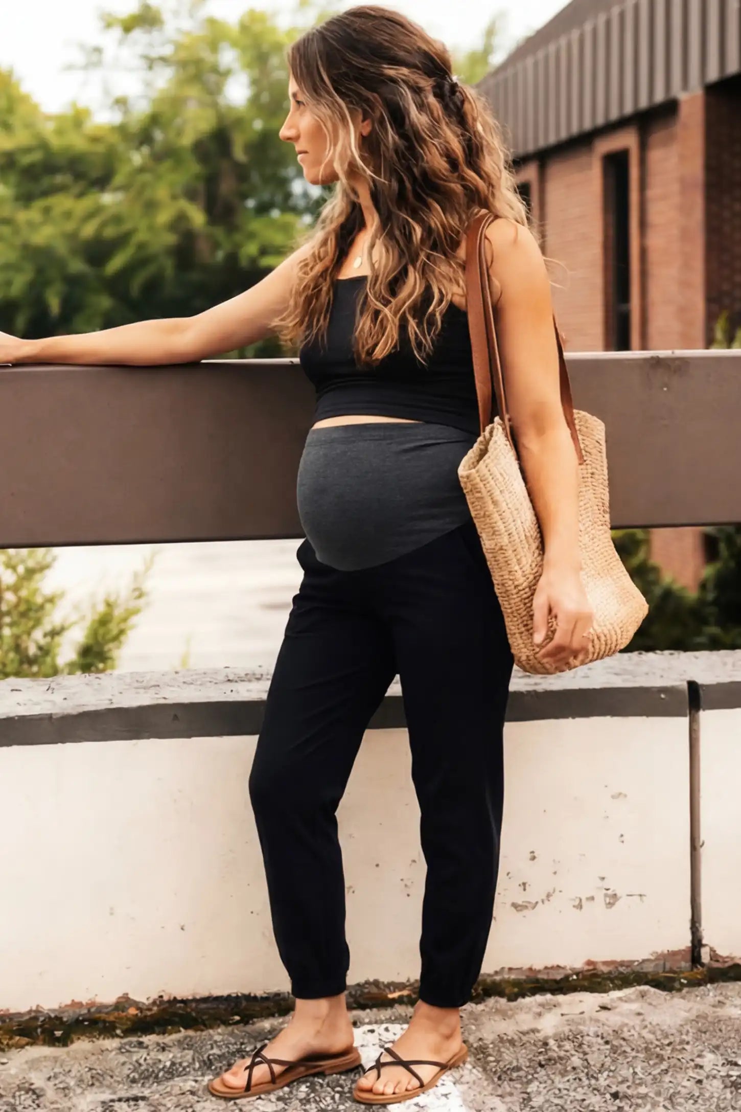 Full Panel Pocketed Maternity Jogger Pants Full Panel Pocketed Maternity Jogger Pants in Black featuring a jersey belly panel on a pregnant woman in outdoor setting, side view.