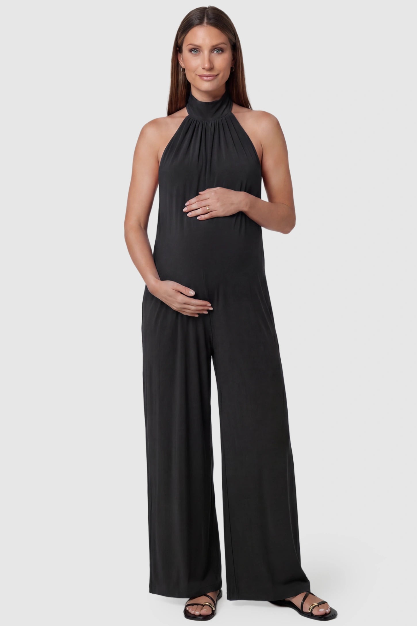 Pocketed Mock Neck Sleeveless Maternity Jumpsuit Pocketed Mock Neck Sleeveless Maternity Jumpsuit in black featuring a high gathered neckline, side pockets shown on a pregnant model, front view.