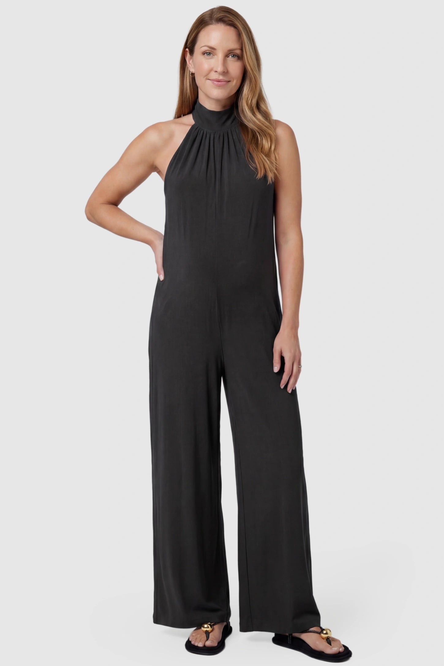 Pocketed Mock Neck Sleeveless Maternity Jumpsuit Pocketed Mock Neck Sleeveless Maternity Jumpsuit in black featuring a high gathered neckline, side pockets shown on a postpartum model, front view.