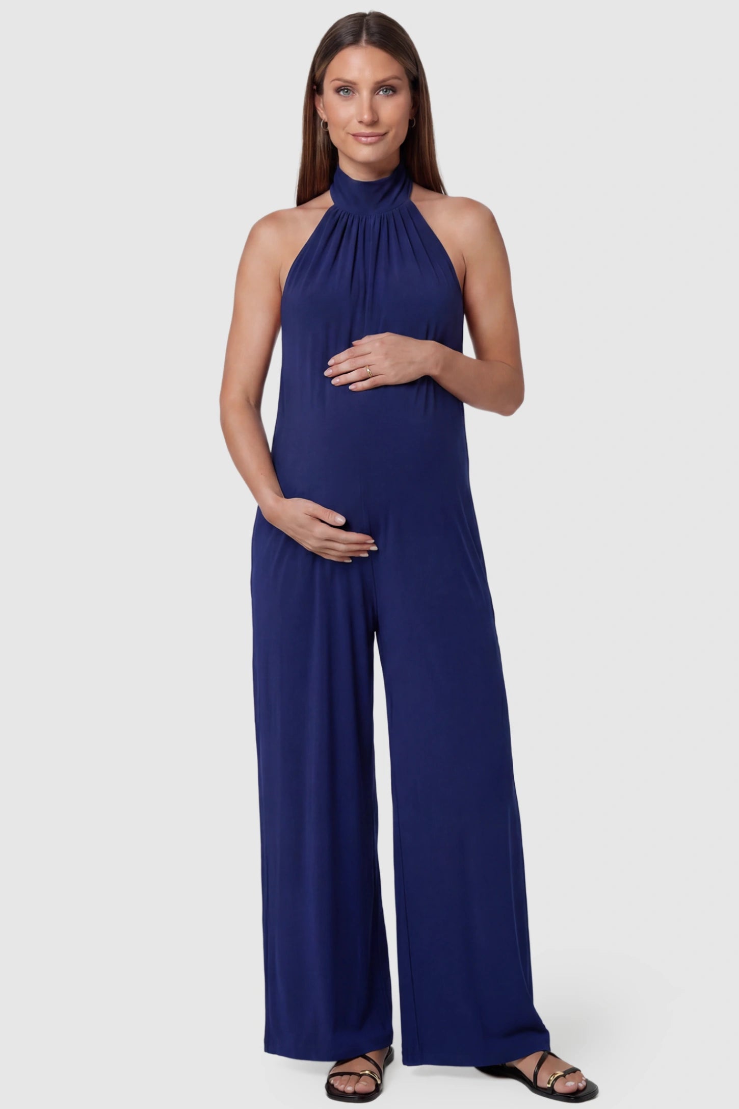 Pocketed Mock Neck Sleeveless Maternity Jumpsuit Pocketed Mock Neck Sleeveless Maternity Jumpsuit in blue featuring a high gathered neckline, side pockets shown on a pregnant model, front view.