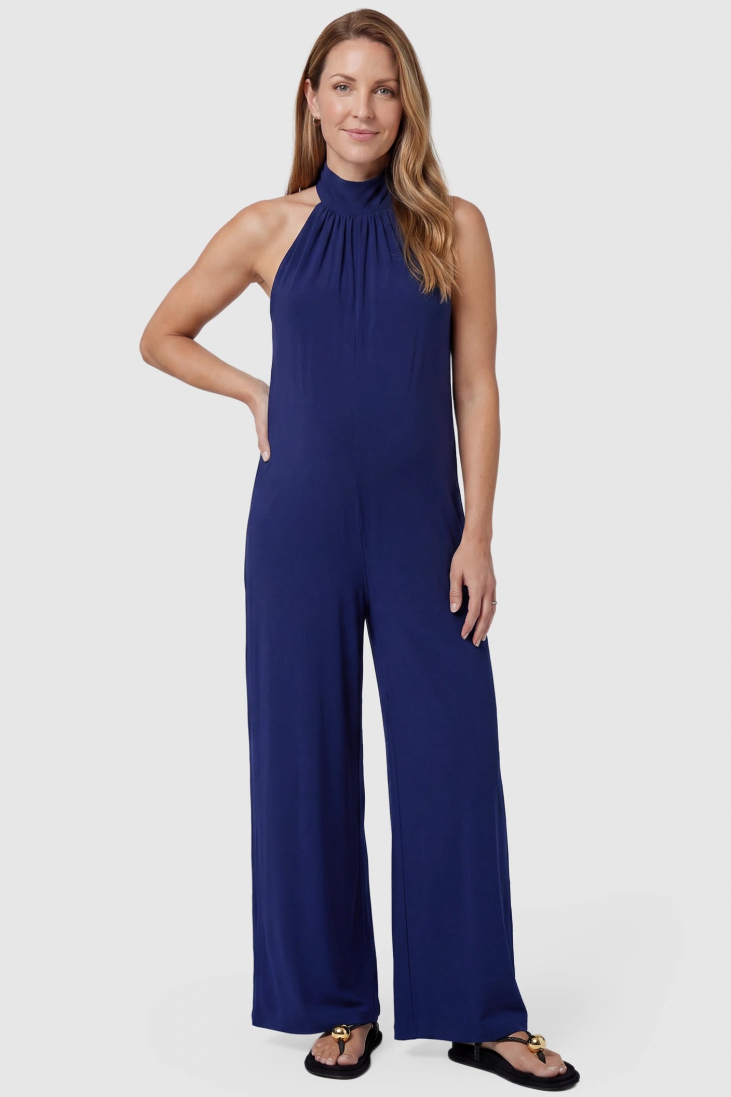 Pocketed Mock Neck Sleeveless Maternity Jumpsuit Pocketed Mock Neck Sleeveless Maternity Jumpsuit in blue featuring a high gathered neckline, side pockets shown on a postpartum model, front view.