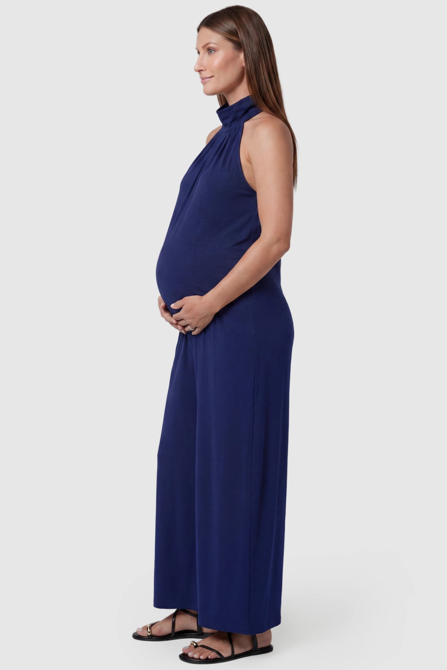 Pocketed Mock Neck Sleeveless Maternity Jumpsuit Pocketed Mock Neck Sleeveless Maternity Jumpsuit in blue featuring a high gathered neckline, side pockets shown on a pregnant model, side view.