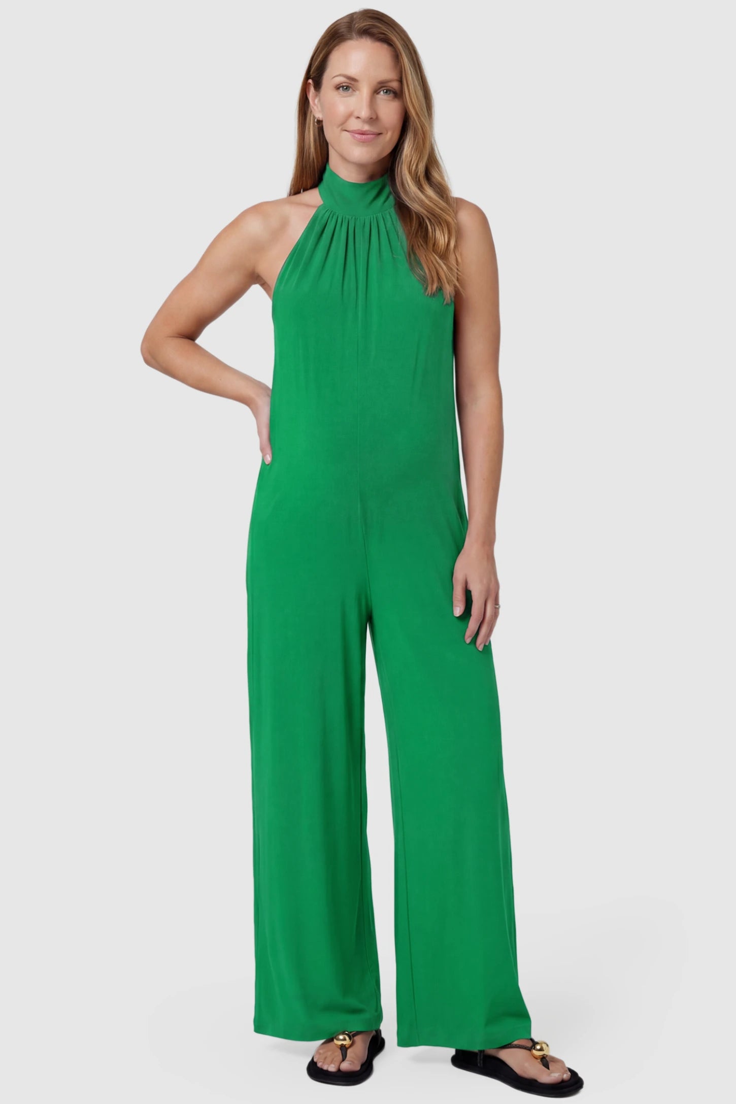 Pocketed Mock Neck Sleeveless Maternity Jumpsuit Pocketed Mock Neck Sleeveless Maternity Jumpsuit in green featuring a high gathered neckline, side pockets shown on a postpartum model, front view.