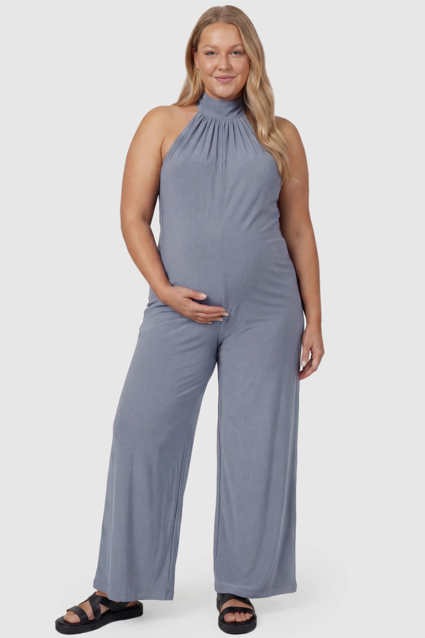 Pocketed Mock Neck Sleeveless Maternity Jumpsuit Pocketed Mock Neck Sleeveless Maternity Jumpsuit in light blue featuring a high gathered neckline, side pockets shown on a plus size pregnant model, front view.