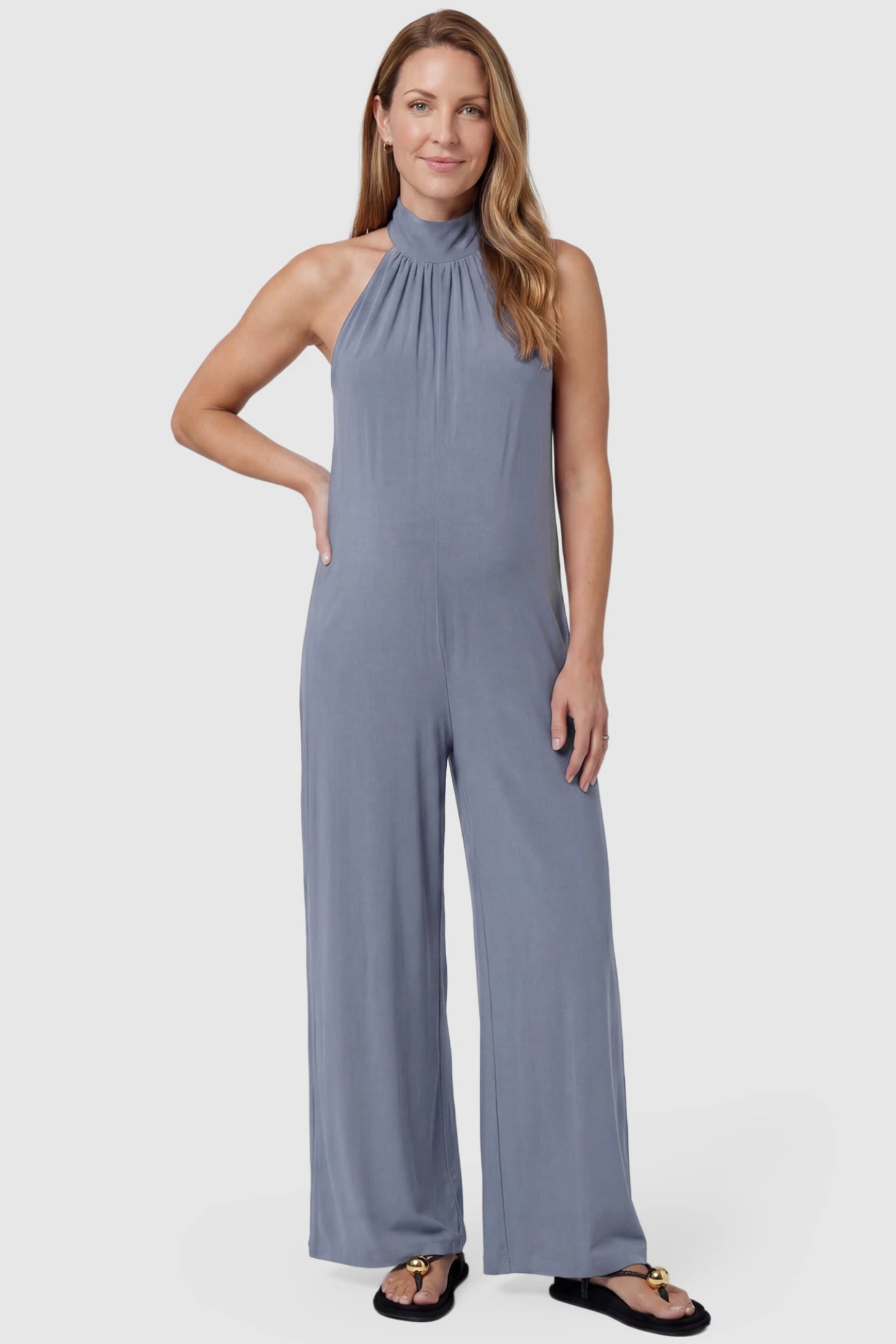 Pocketed Mock Neck Sleeveless Maternity Jumpsuit Pocketed Mock Neck Sleeveless Maternity Jumpsuit in light blue featuring a high gathered neckline, side pockets shown on a postpartum model, front view.