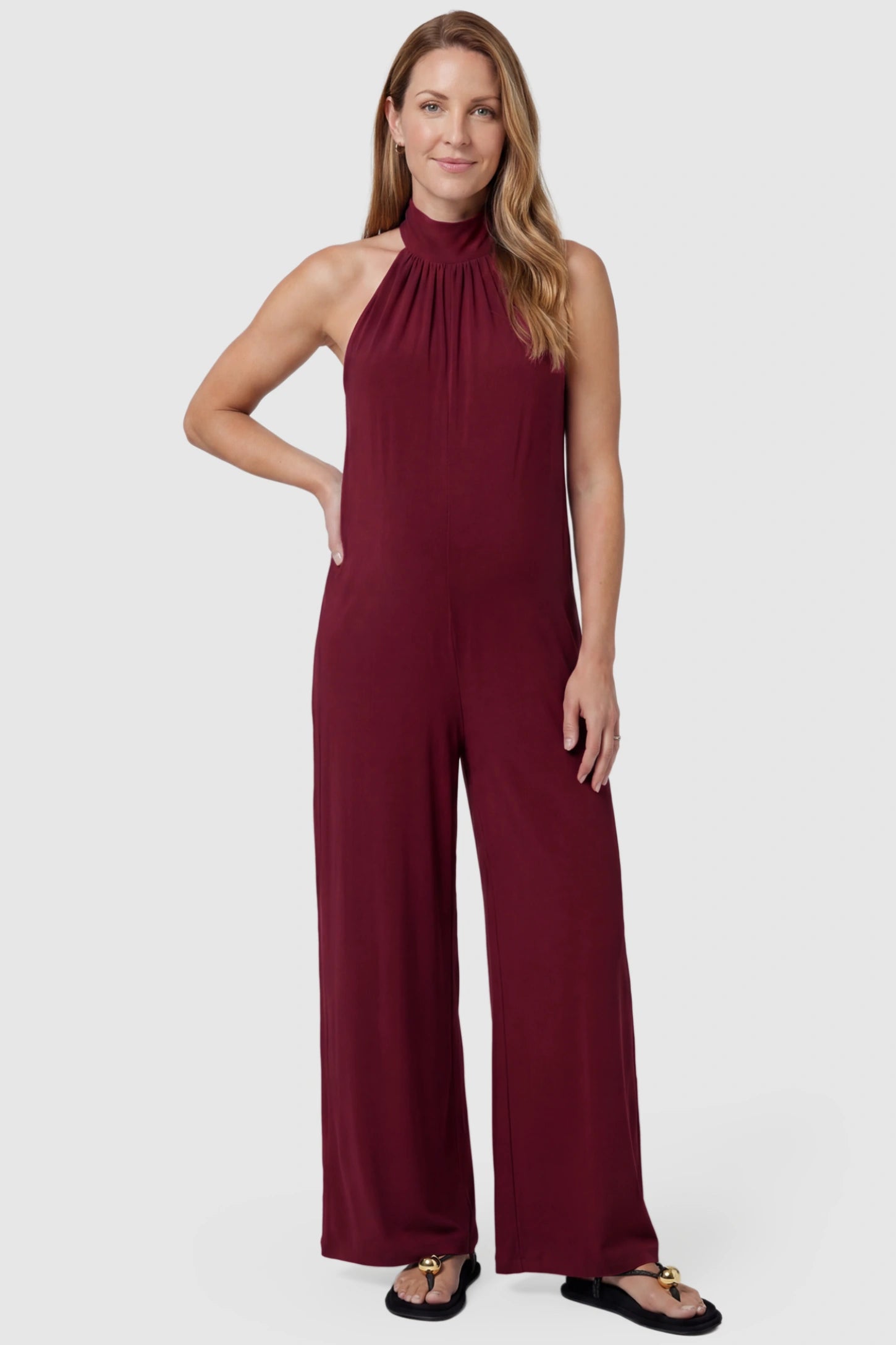 Pocketed Mock Neck Sleeveless Maternity Jumpsuit Pocketed Mock Neck Sleeveless Maternity Jumpsuit in rose red featuring a high gathered neckline, side pockets shown on a postpartum model, front view.