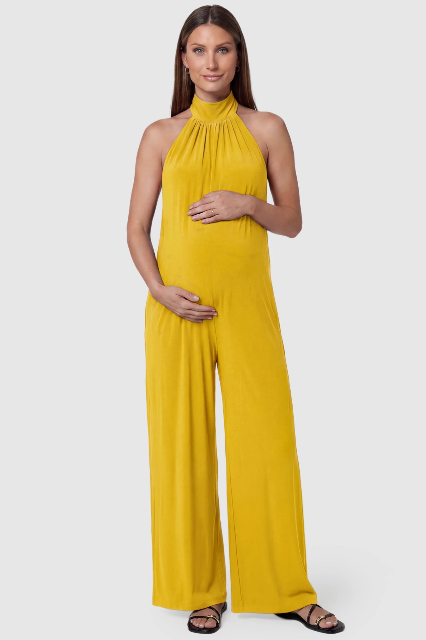 Pocketed Mock Neck Sleeveless Maternity Jumpsuit Pocketed Mock Neck Sleeveless Maternity Jumpsuit in yellow featuring a high gathered neckline, side pockets shown on a pregnant model, front view.