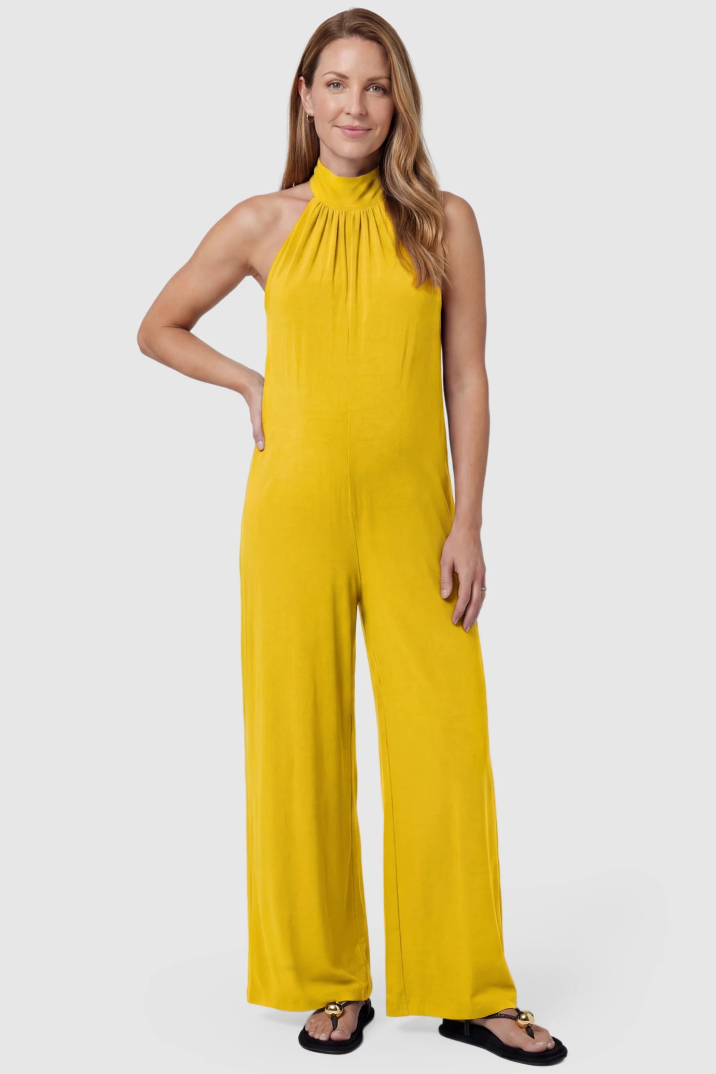 Pocketed Mock Neck Sleeveless Maternity Jumpsuit Pocketed Mock Neck Sleeveless Maternity Jumpsuit in yellow featuring a high gathered neckline, side pockets shown on a postpartum model, front view.