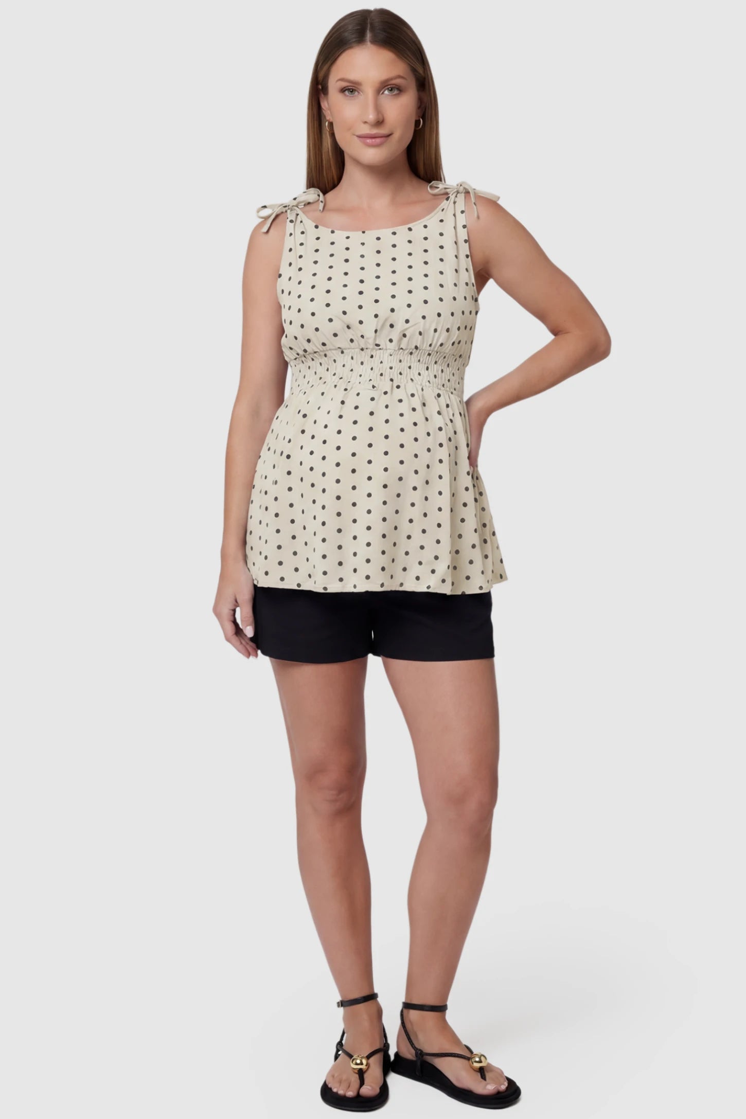 Polka Dot Round Neck Flowy Maternity Top Polka Dot Flowy Maternity Top in Beige featuring a smocked elastic waistband and shoulder ties on a pregnant model, full body view.