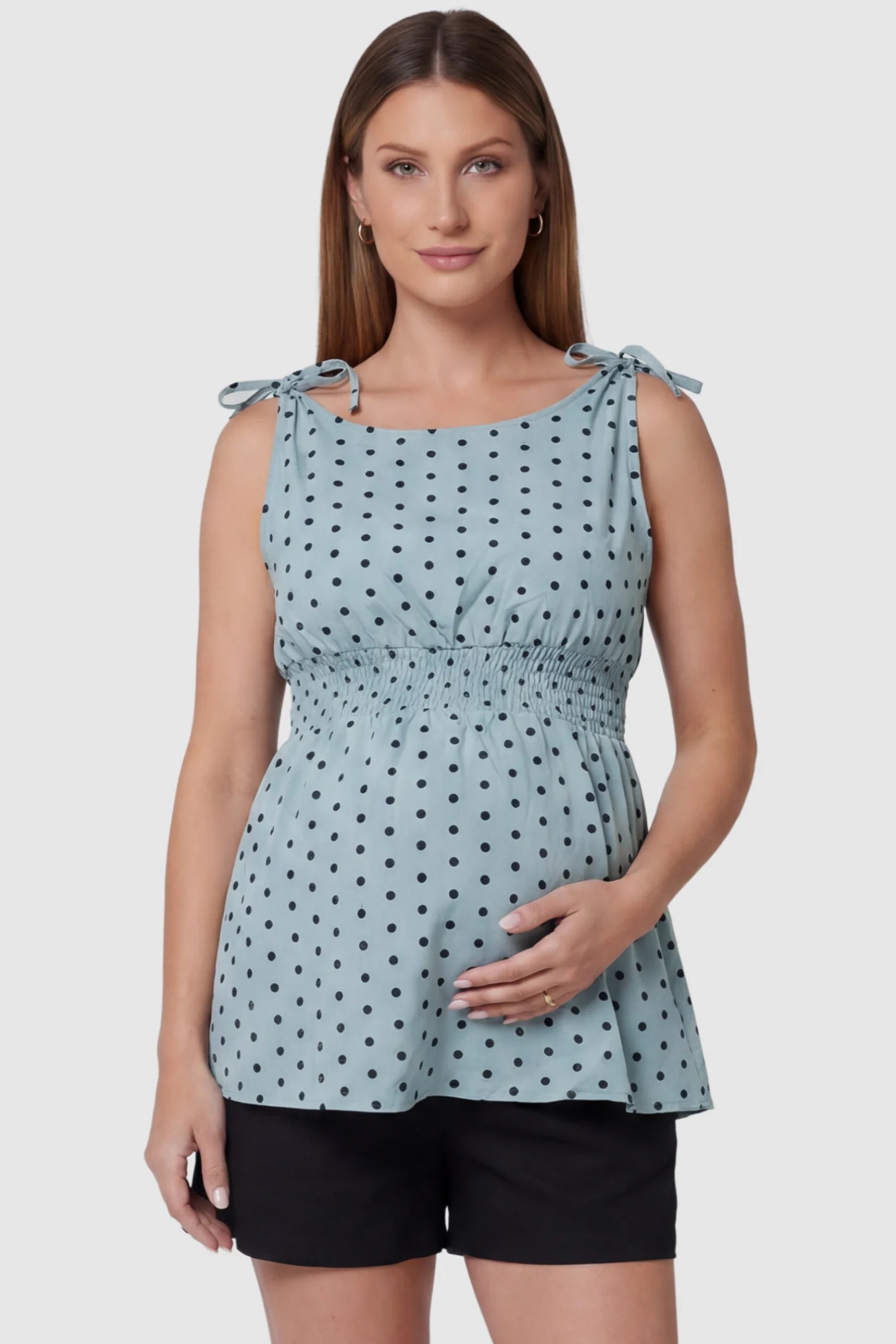 Polka Dot Round Neck Flowy Maternity Top Polka Dot Flowy Maternity Top in Blue featuring a smocked elastic waistband and shoulder ties on a pregnant model, front view.