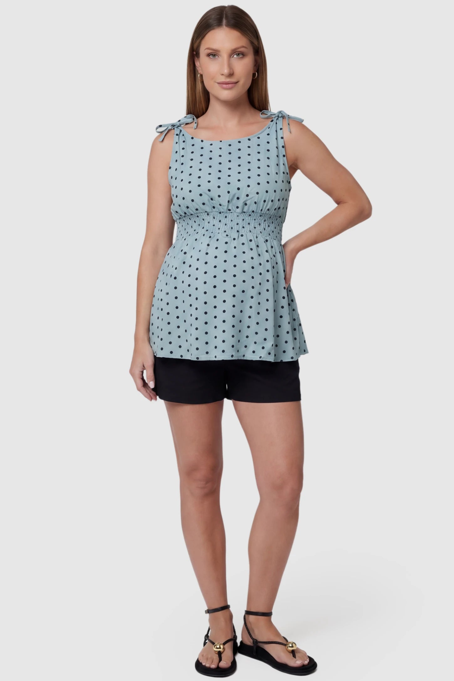 Polka Dot Round Neck Flowy Maternity Top Polka Dot Flowy Maternity Top in Blue featuring a smocked elastic waistband and shoulder ties on a pregnant model, full body view.