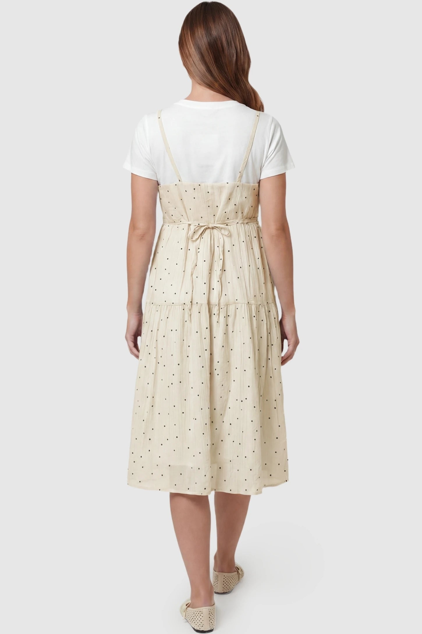 Polka Dot Round Neck Tiered Midi Maternity Dress Polka Dot Round Neck Tiered Midi Maternity Dress in Beige featuring a self-tie back bow and thin adjustable straps on a pregnant model, back view.