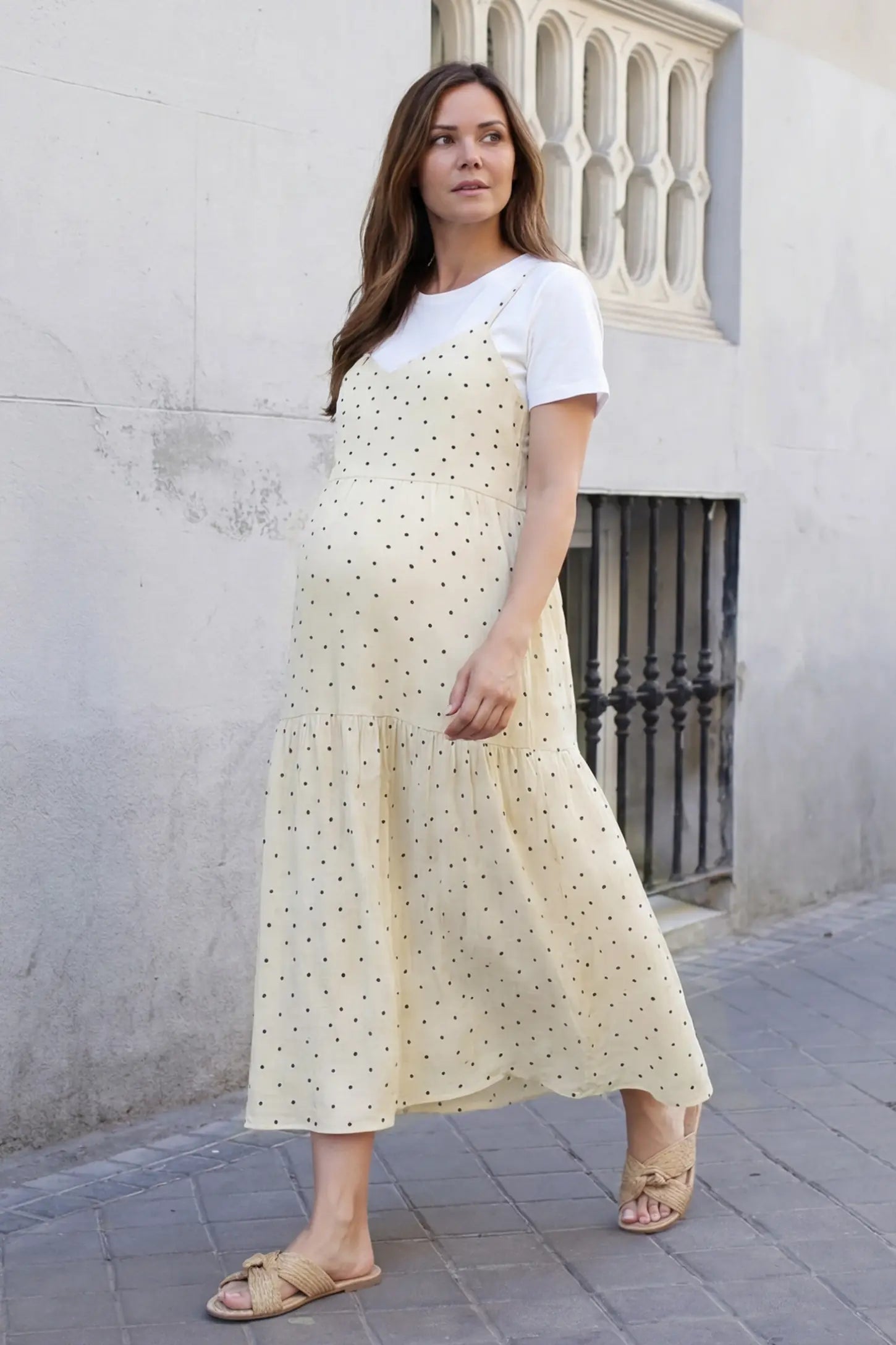 Polka Dot Round Neck Tiered Midi Maternity Dress olka Dot Round Neck Tiered Midi Maternity Dress in Beige featuring a breezy tiered midi length paired with woven sandals on a pregnant model, lifestyle view.