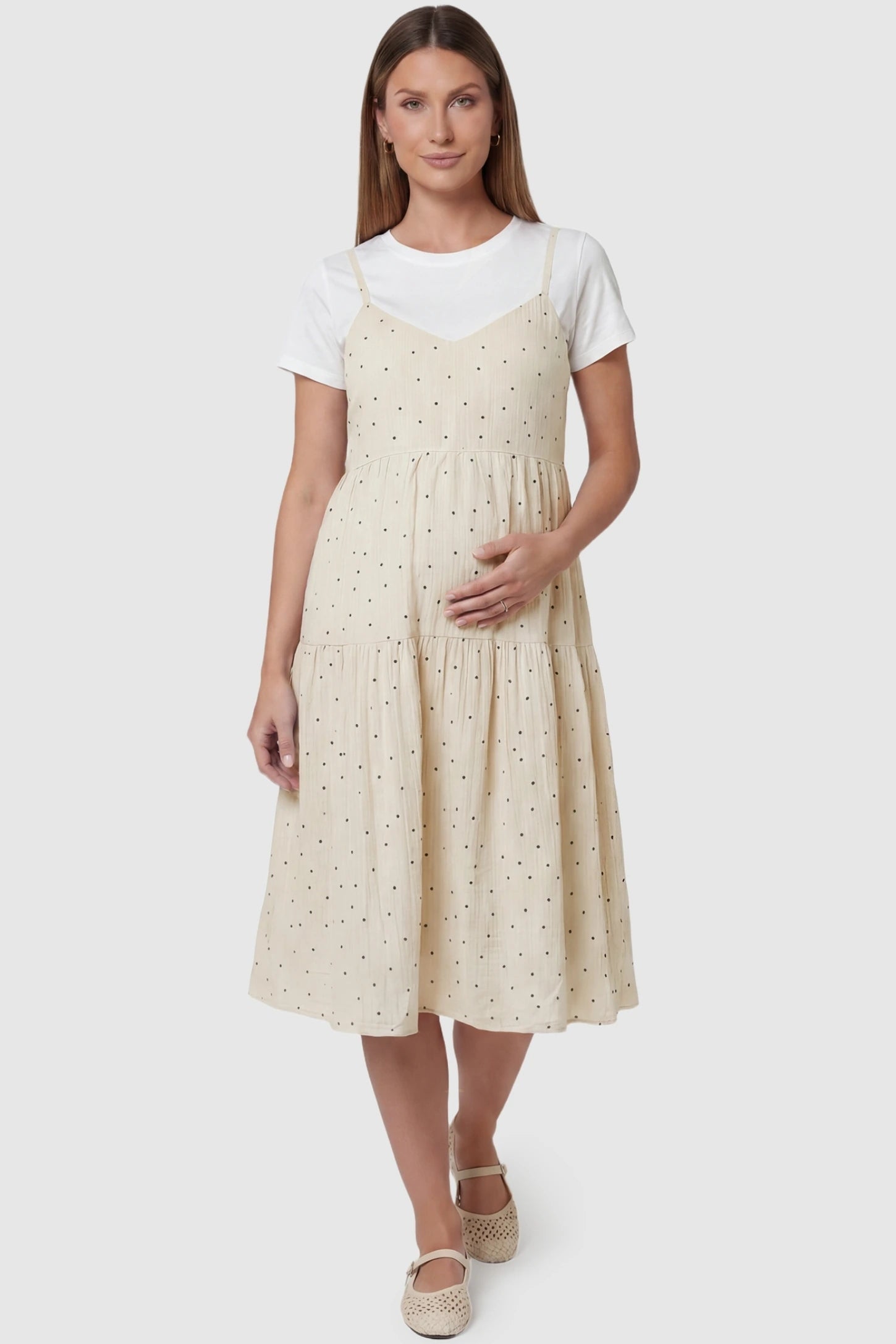 Polka Dot Round Neck Tiered Midi Maternity Dress Polka Dot Round Neck Tiered Midi Maternity Dress in Beige featuring a V-neckline slip-style over a white tee on a pregnant model, front view.