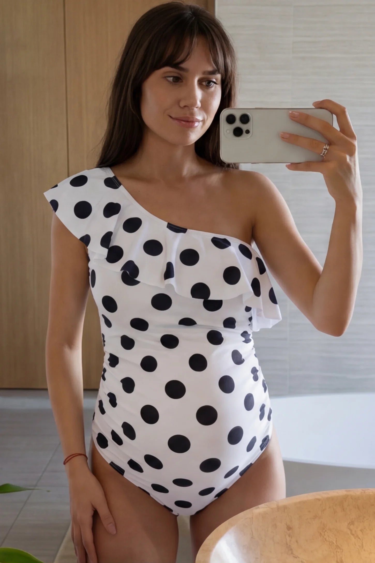 Polka Dot Side Ruched One-Shoulder Maternity Swimsuit Polka Dot Side Ruched One-Shoulder Maternity Swimsuit in White featuring side ruched panels and ruffle detail on a pregnant model in indoor setting, front view.
