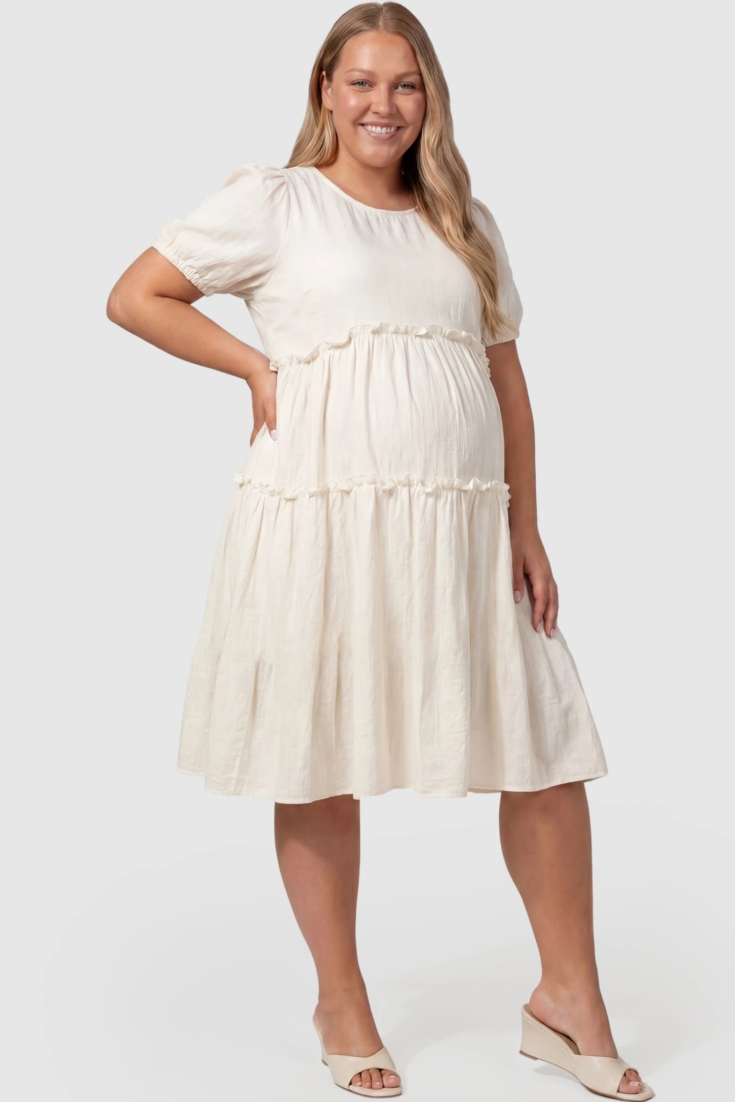 Puff Sleeve Tiered Midi Maternity Dress Puff Sleeve Tiered Midi Maternity Dress in Off-White featuring ruffled tiered skirt on a pregnant plus-size model, front view.