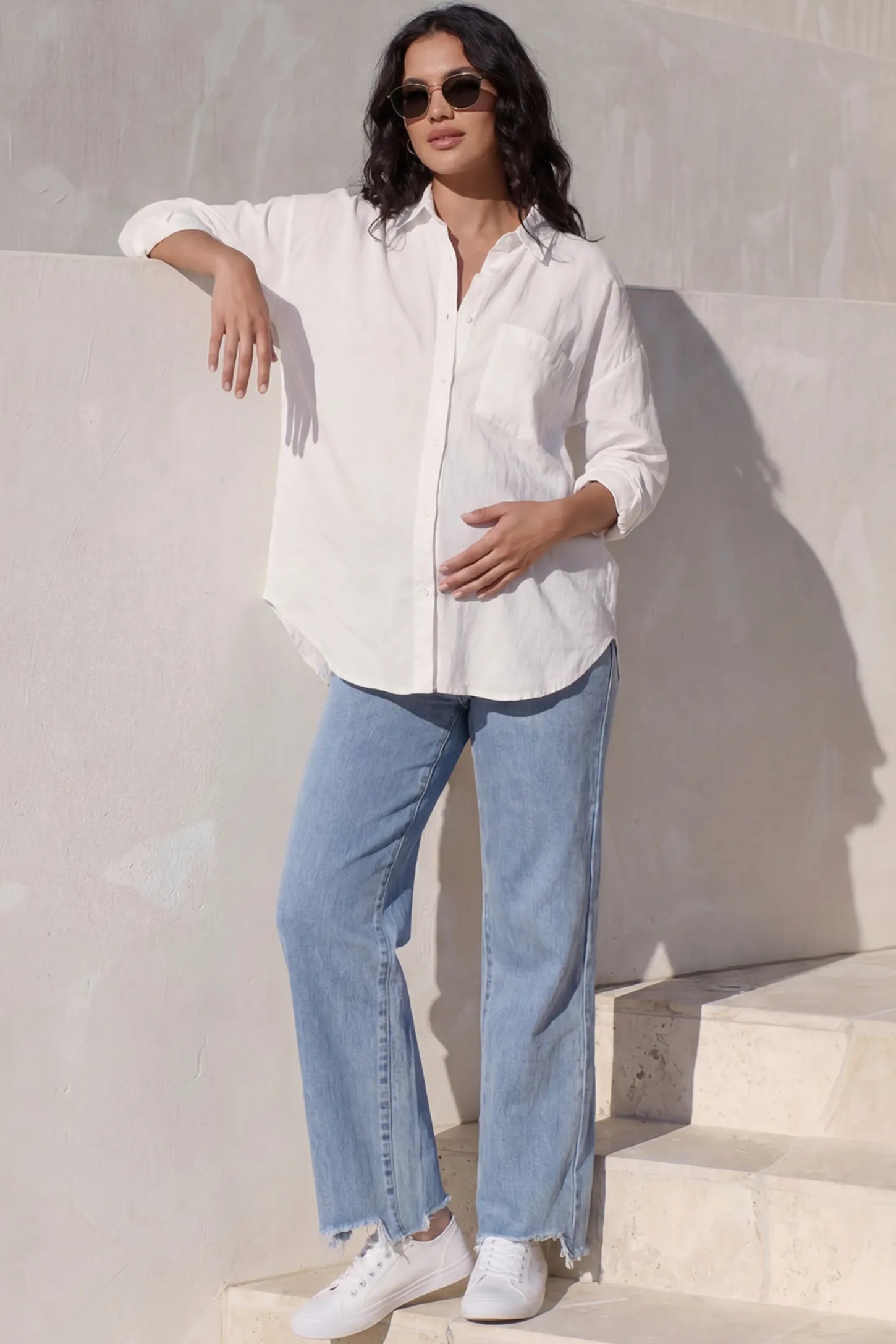 Raw Hem Wide Leg Maternity Jeans Raw Hem Wide Leg Maternity Jeans in Light Blue Denim with a grey over-the-belly comfort panel and raw hem on a pregnant woman showing front.