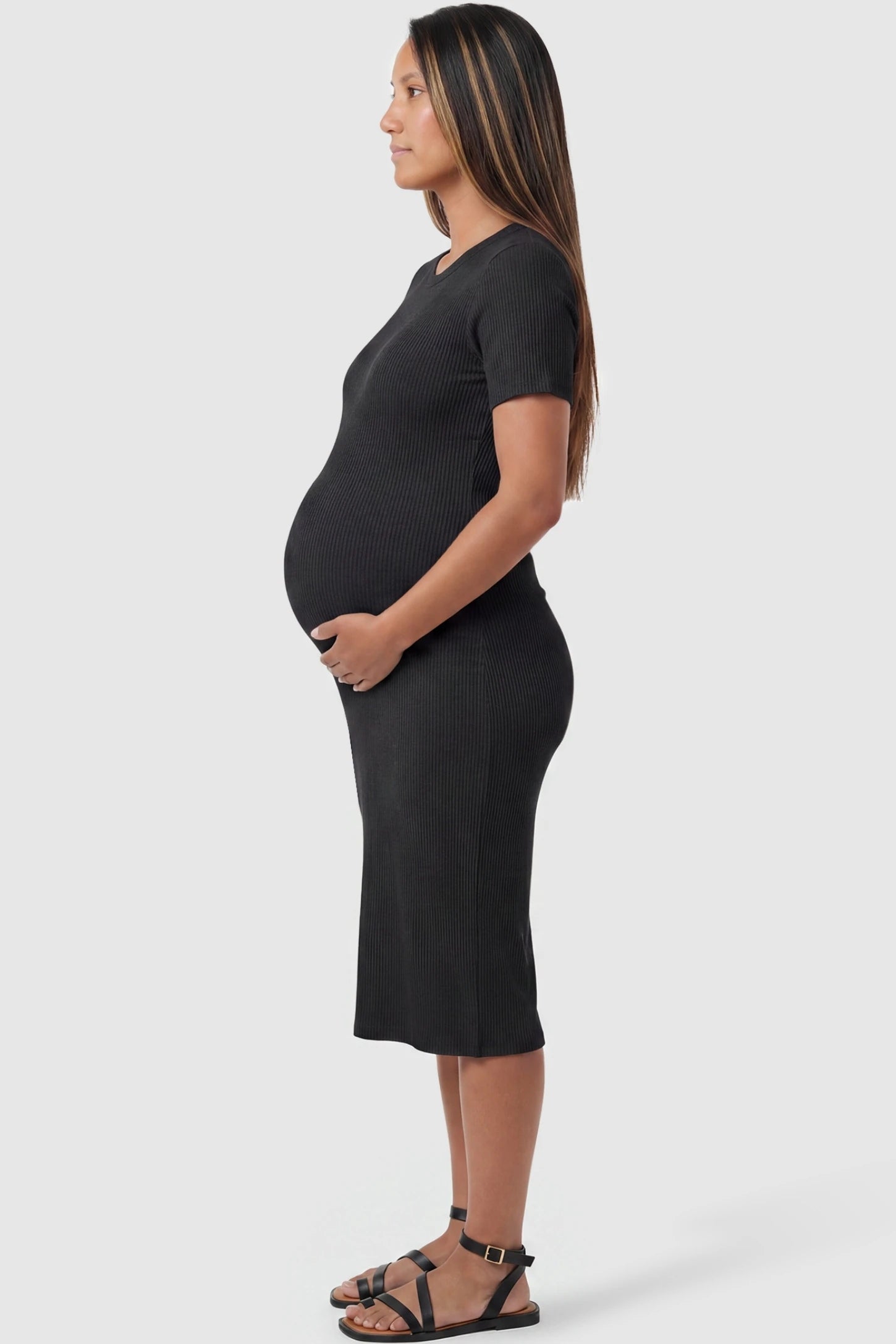 Ribbed Knit Short Sleeve Midi Maternity Dress Ribbed Knit Short Sleeve Midi Maternity Dress in Black featuring a stretchy bump-hugging silhouette on a pregnant model, side view.