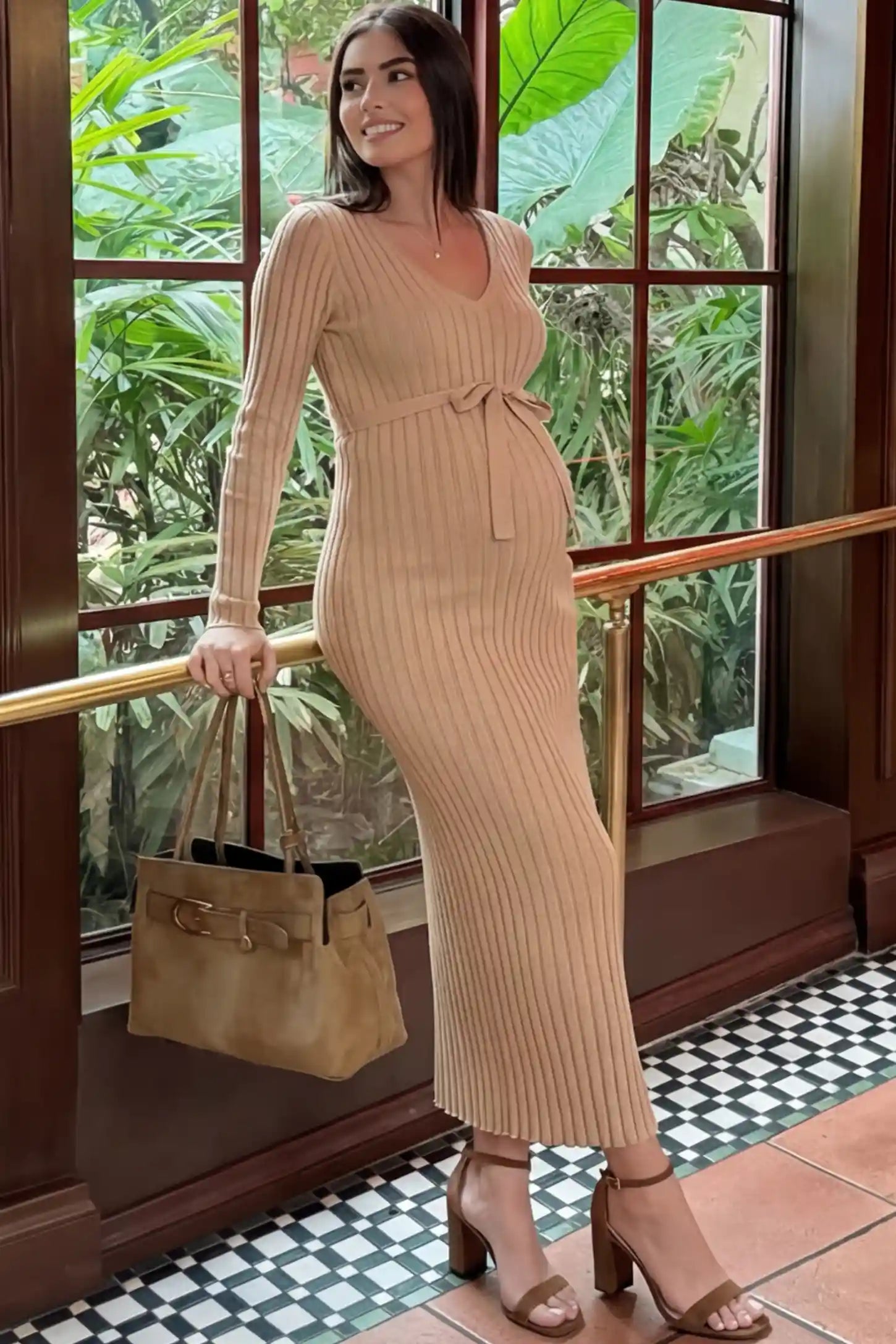 Ribbed Knit V-Neck Tie Waist Maternity Maxi Dress Ribbed knit maternity maxi dress in beige featuring a V-neck and tie waist on a model in an indoor setting, side view.