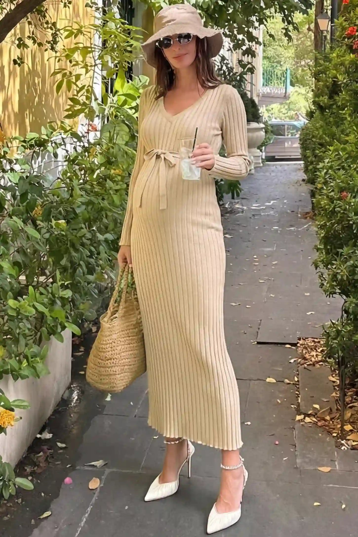 Ribbed knit maternity maxi dress in beige featuring a V-neck and tie waist on a model in an outdoor setting, front view.