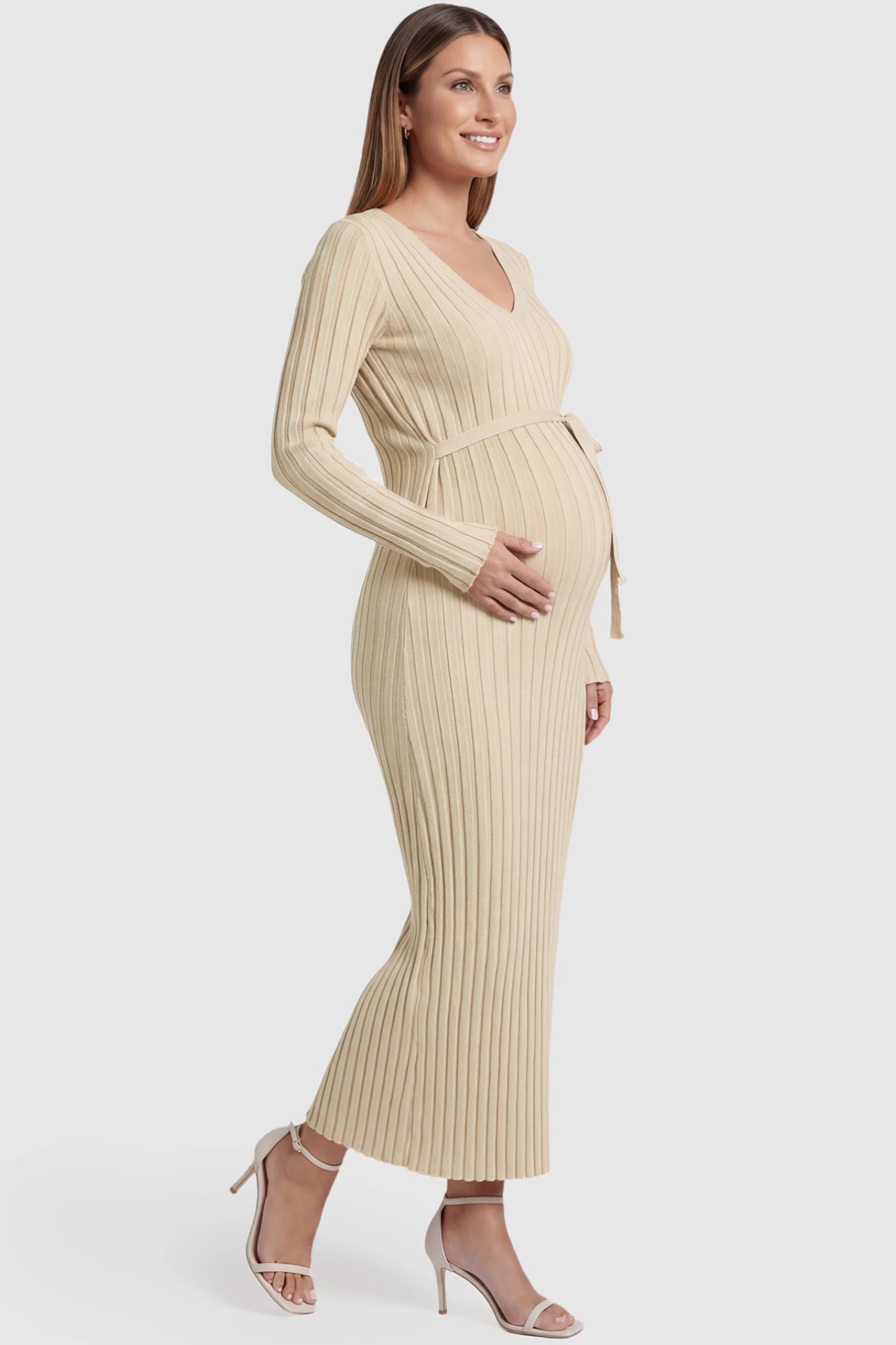 Ribbed Knit V-Neck Tie Waist Maternity Maxi Dress Ribbed Knit V-Neck Maternity Maxi Dress in Beige featuring a tie waist and long sleeves on a pregnant model, side view.