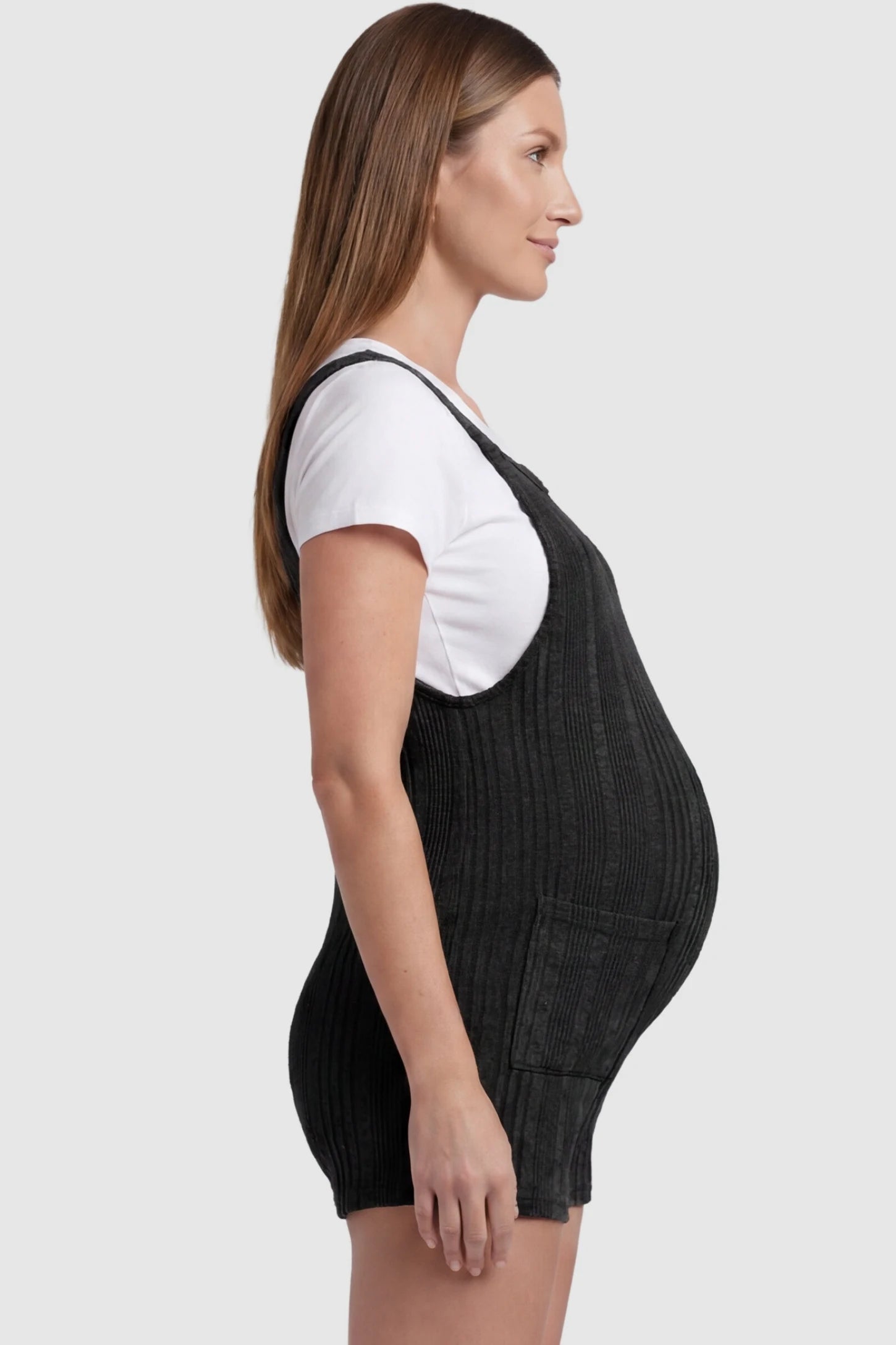 Ribbed Pocket Knit Romper in Black featuring a flexible ribbed knit fabric on a pregnant model, side view.