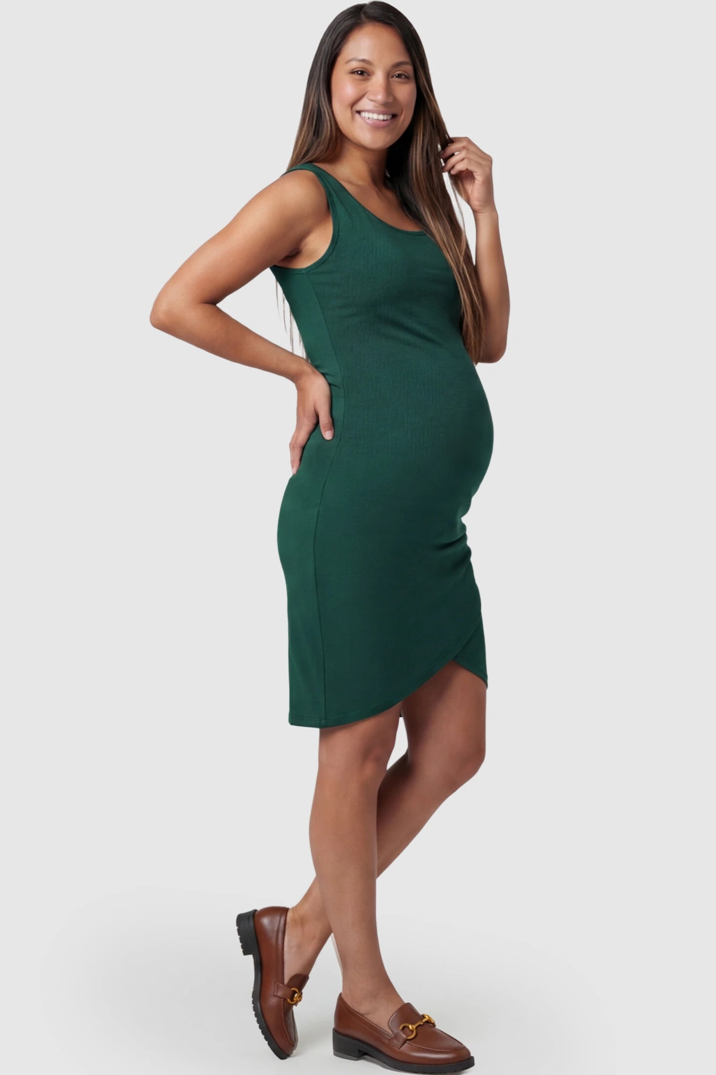 Ruched Tulip-Hem Sleeveless Bodycon Maternity Dress Ruched Tulip-Hem Bodycon Maternity Dress in Dark Green featuring a side-ruched pencil skirt on a pregnant model posing side.