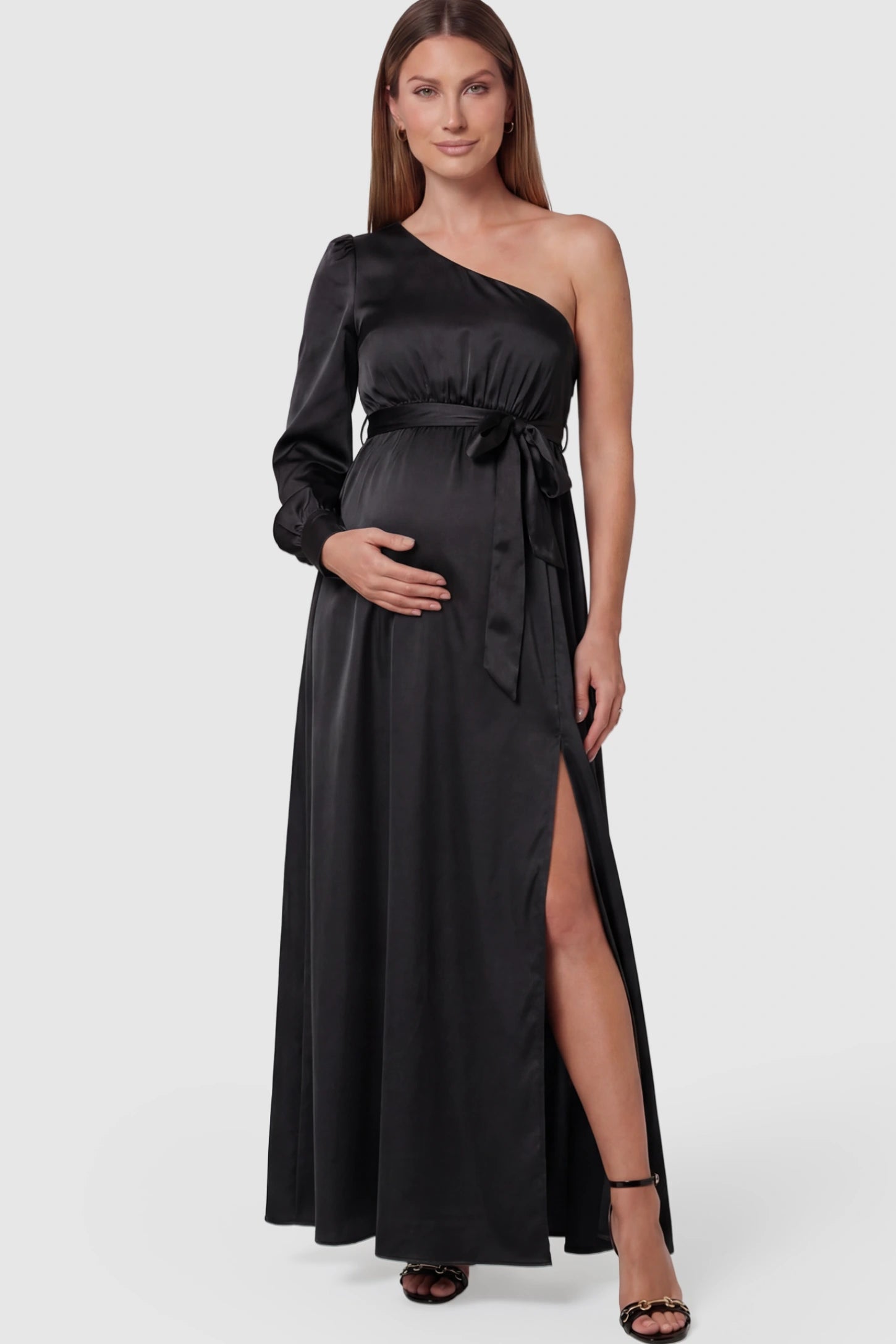 Satin One Shoulder Belted Maternity Maxi Dress Satin One-Shoulder Belted Maternity Maxi Dress in black featuring a side slit and waist tie on a pregnant model posing front.