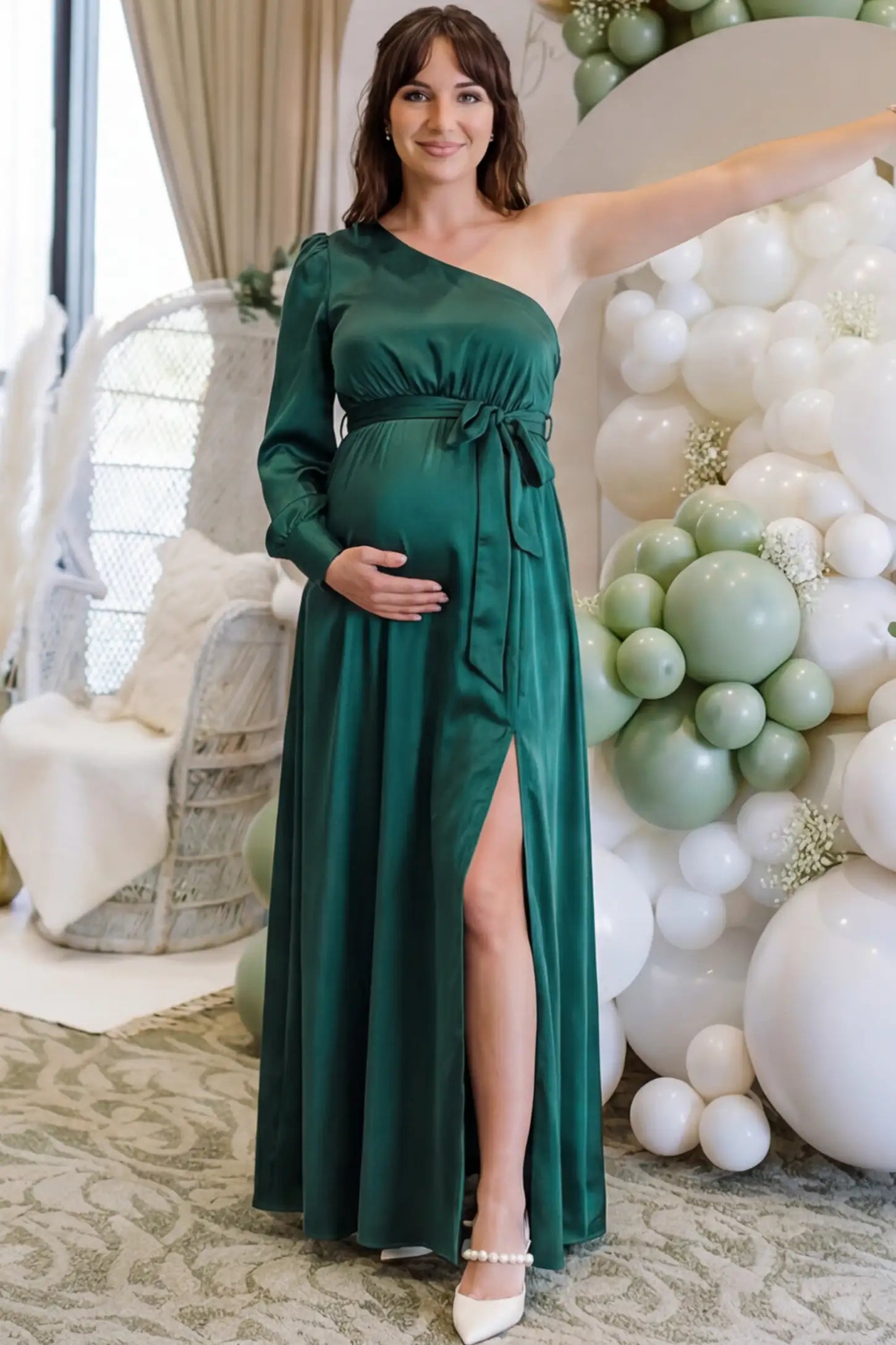 Satin One Shoulder Belted Maternity Maxi Dress Satin One-Shoulder Belted Maternity Maxi Dress in Green featuring a side slit and waist tie on a pregnant woman during outdoor photoshoot front view.