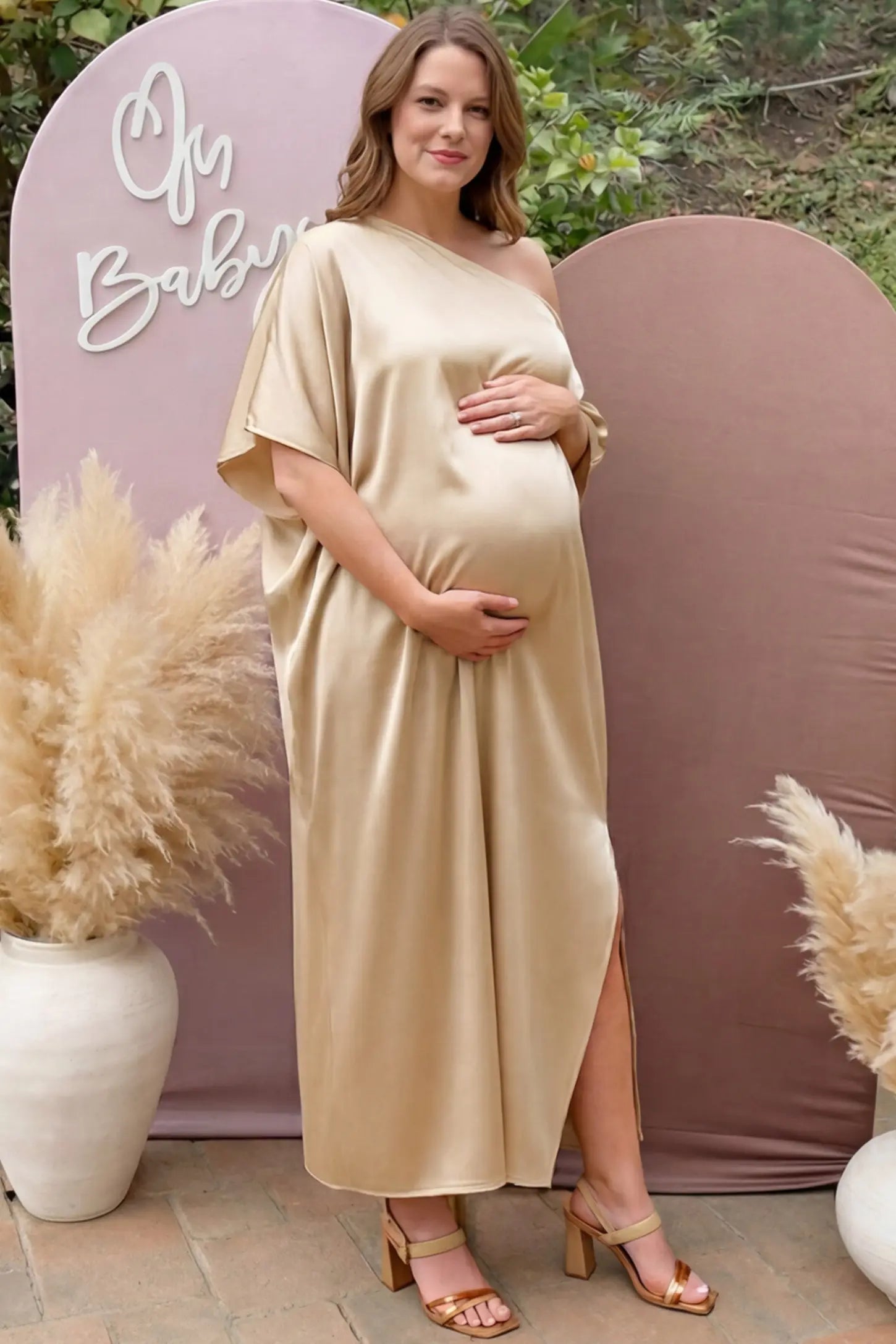 Satin One Shoulder Side Slit Maternity Maxi Dress in Apricot featuring a draped batwing sleeve on a pregnant woman in outdoor setting, front view.