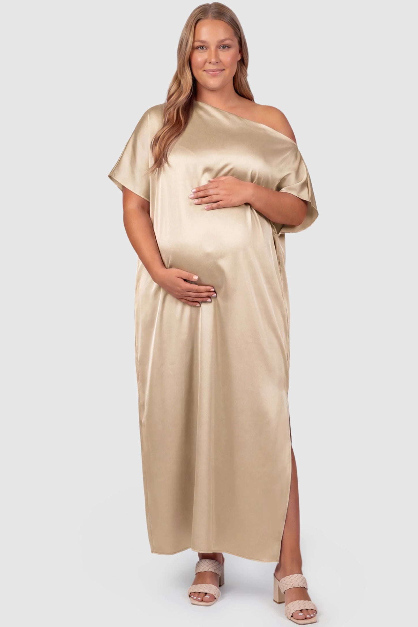 Satin One Shoulder Side Slit Maternity Maxi Dress Satin One Shoulder Side Slit Maternity Maxi Dress in Apricot featuring a draped batwing sleeve on a plus size pregnant model, front view.