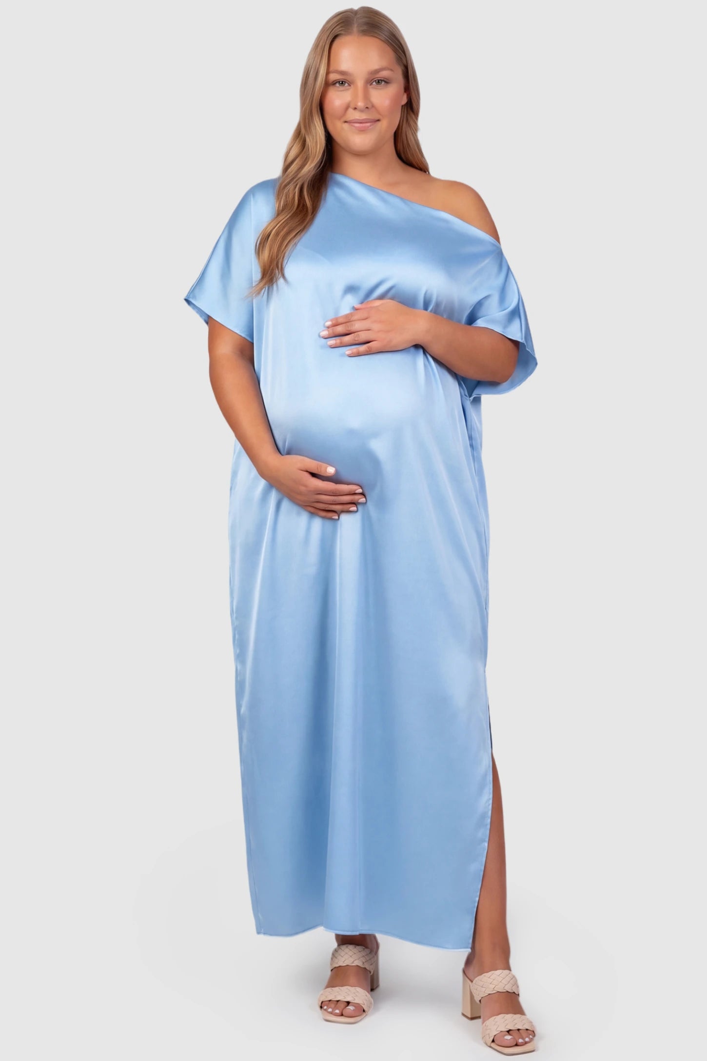 Satin One Shoulder Side Slit Maternity Maxi Dress Satin One Shoulder Side Slit Maternity Maxi Dress in Blue featuring a draped batwing sleeve on a plus size pregnant model, front view.