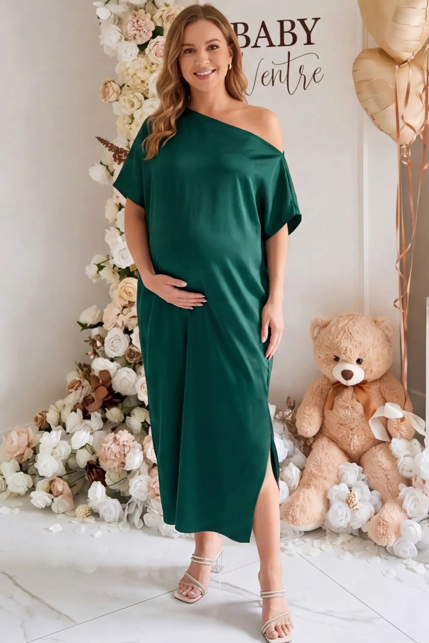 Satin One Shoulder Side Slit Maternity Maxi Dress Satin One Shoulder Side Slit Maternity Maxi Dress in Dark Green featuring a draped batwing sleeve on a pregnant woman in indoor setting, front view.
