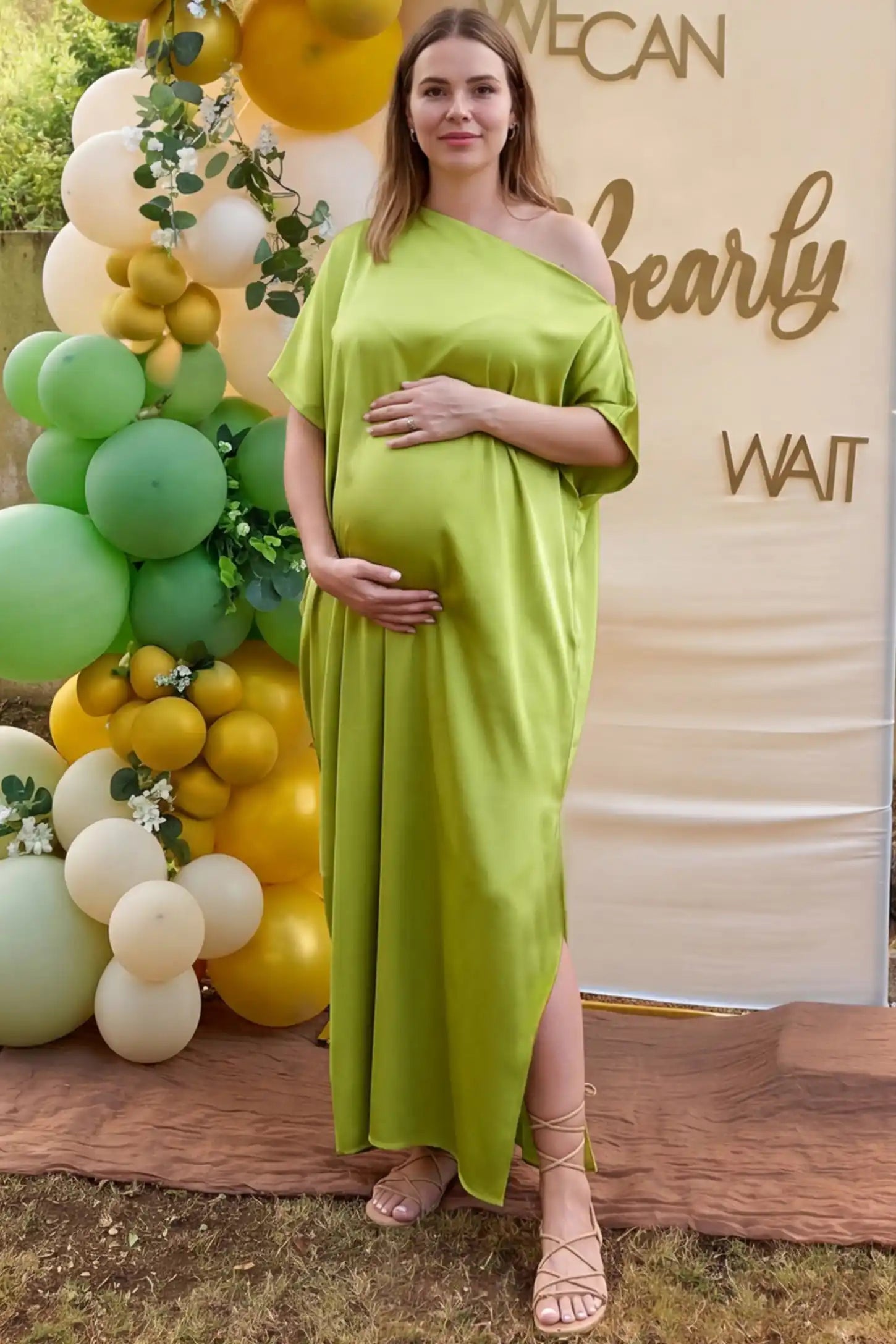 Satin One Shoulder Side Slit Maternity Maxi Dress Satin One Shoulder Side Slit Maternity Maxi Dress in Green featuring a draped batwing sleeve on a pregnant woman in outdoor setting, front view.
