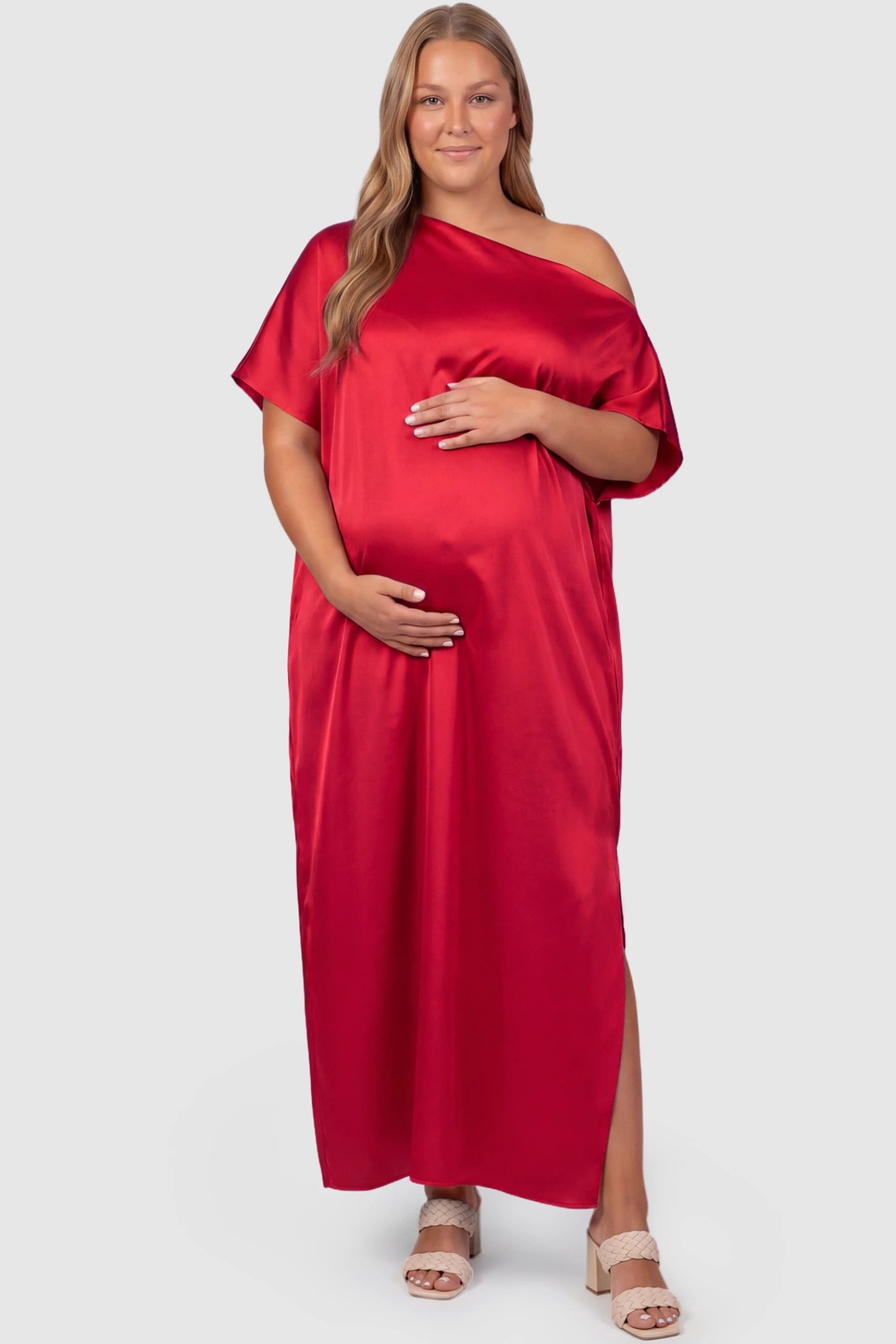 Satin One Shoulder Side Slit Maternity Maxi Dress Satin One Shoulder Side Slit Maternity Maxi Dress in Red featuring a draped batwing sleeve on a plus size pregnant model, front view.
