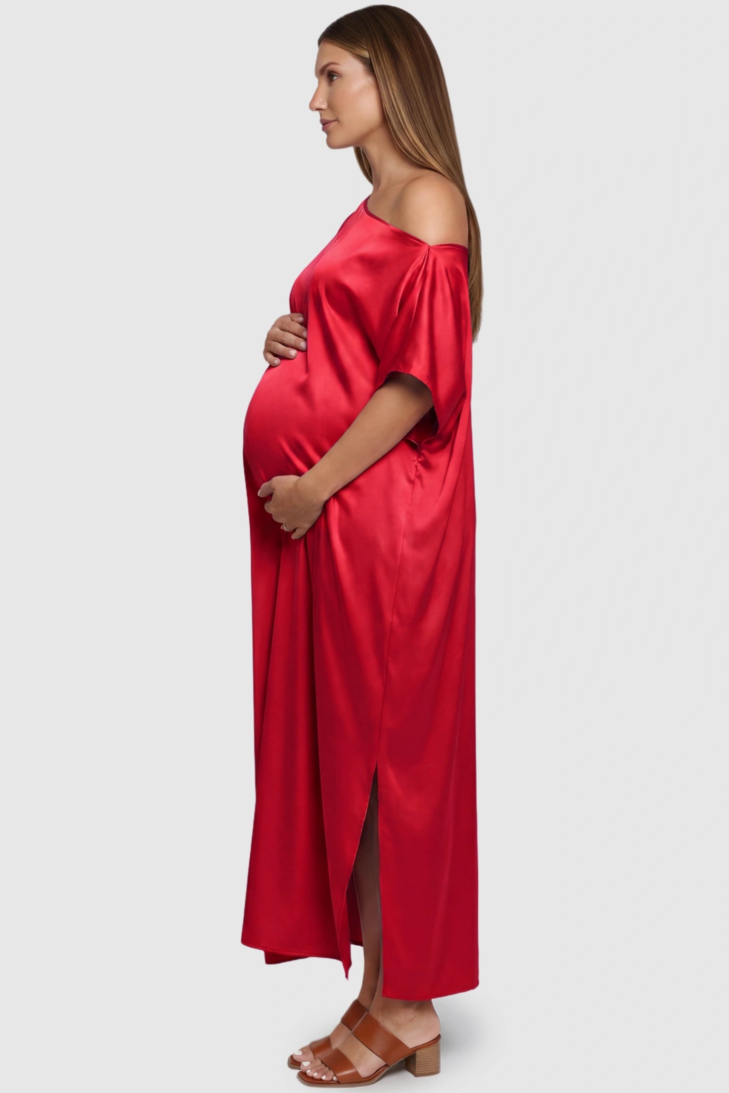 Satin One Shoulder Side Slit Maternity Maxi Dress Satin One Shoulder Side Slit Maternity Maxi Dress in Red featuring a draped batwing sleeve on a pregnant model, side view.