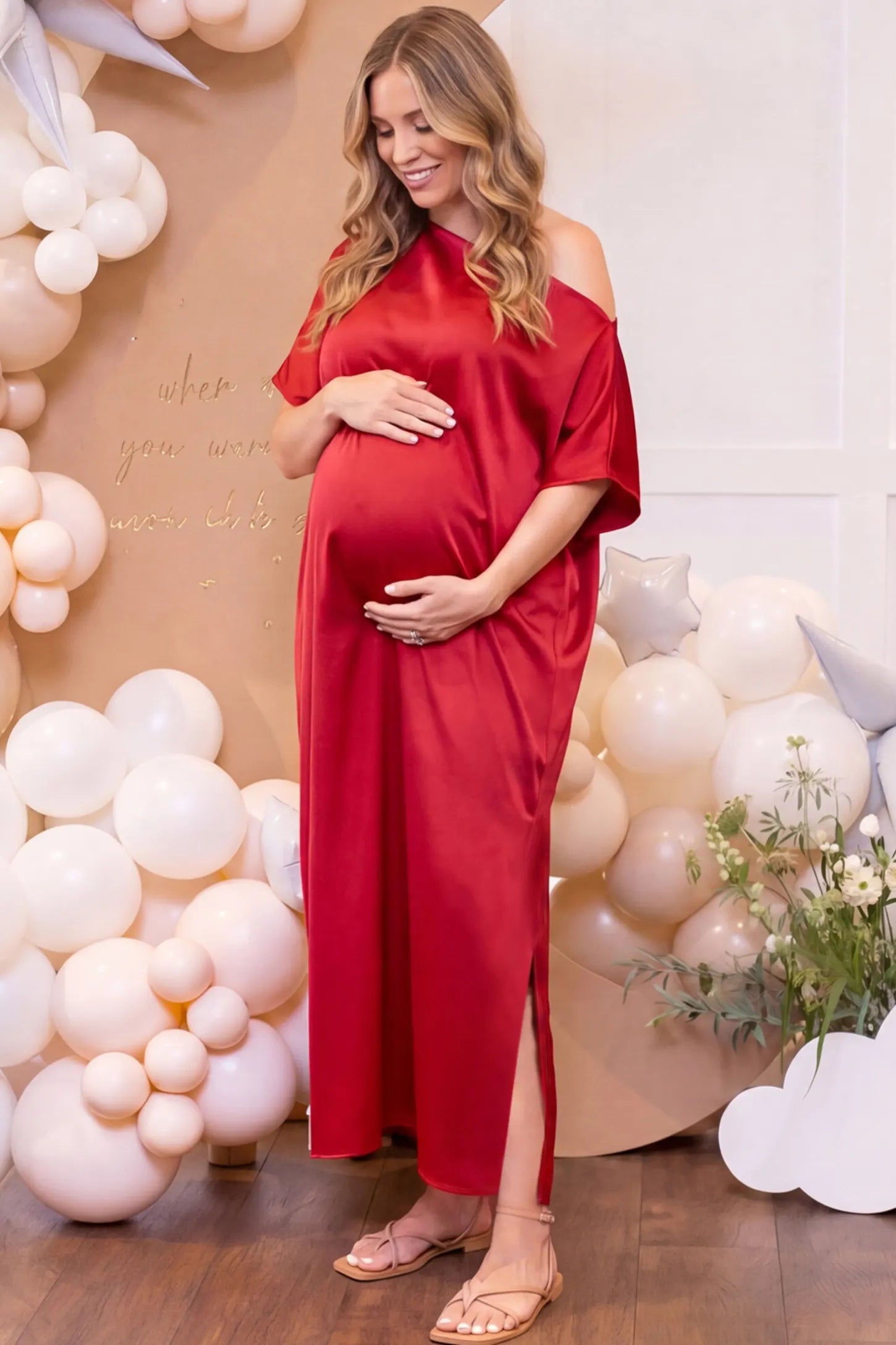 Satin One Shoulder Side Slit Maternity Maxi Dress Satin One Shoulder Side Slit Maternity Maxi Dress in Red featuring a draped batwing sleeve on a pregnant woman in indoor setting, side view.