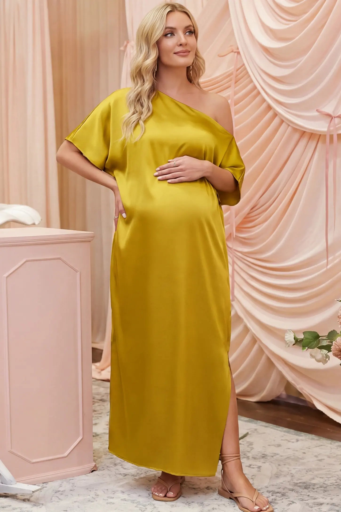 Satin One Shoulder Side Slit Maternity Maxi Dress Satin One Shoulder Side Slit Maternity Maxi Dress in Yellow featuring a draped batwing sleeve on a pregnant woman in indoor setting, front view.