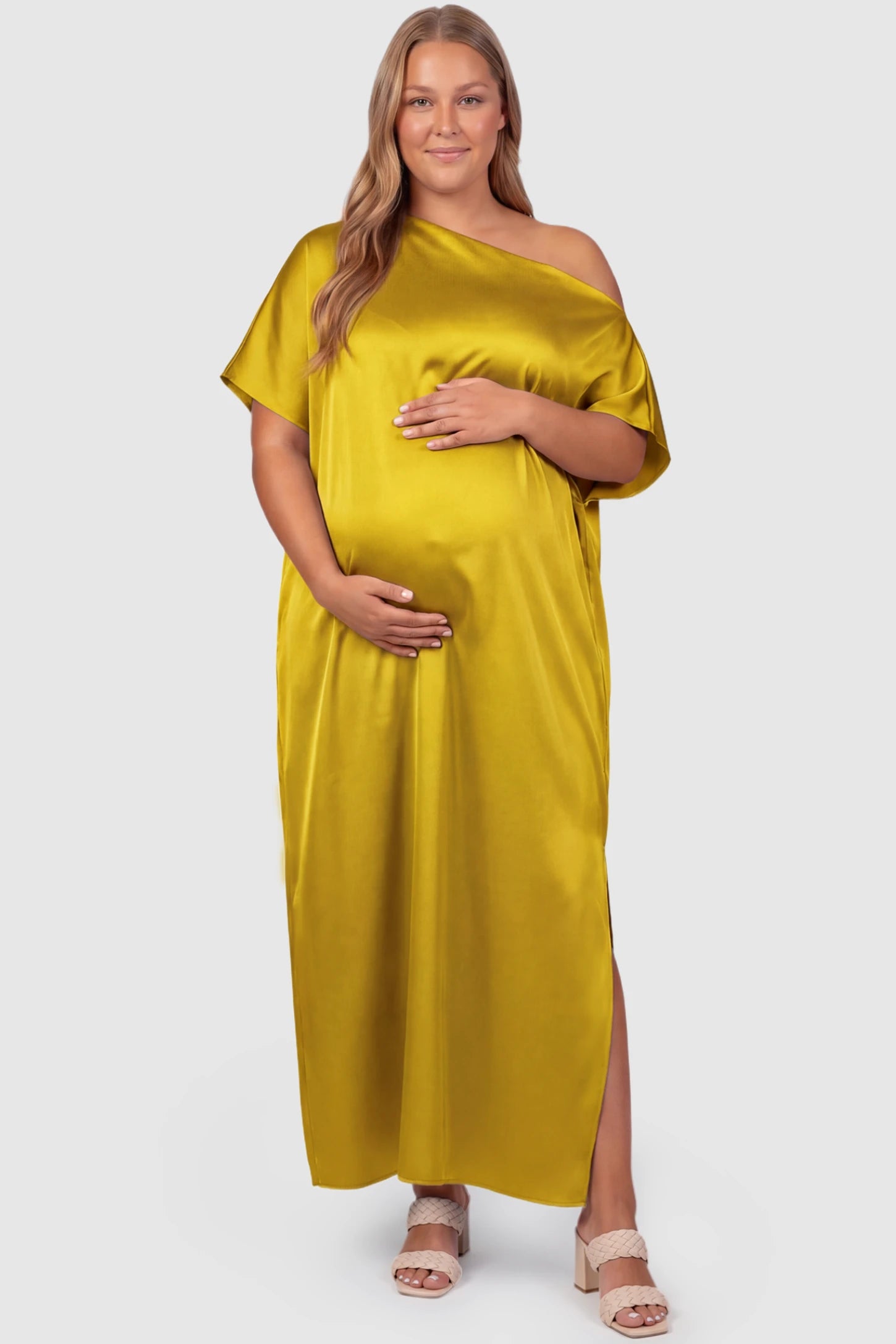 Satin One Shoulder Side Slit Maternity Maxi Dress Satin One Shoulder Side Slit Maternity Maxi Dress in Yellow featuring a draped batwing sleeve on a plus size pregnant model, front view.