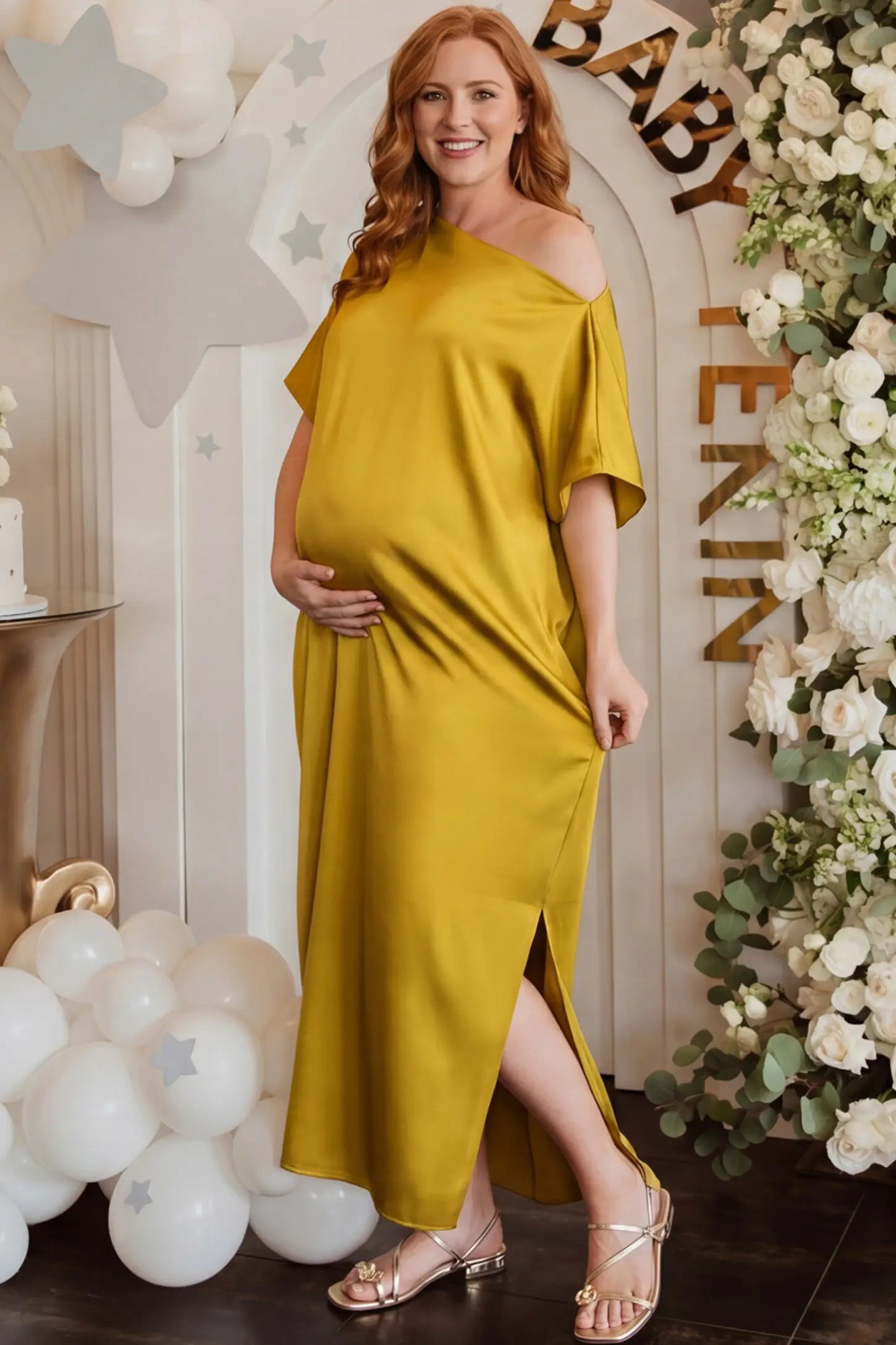 Satin One Shoulder Side Slit Maternity Maxi Dress Satin One Shoulder Side Slit Maternity Maxi Dress in Yellow featuring a draped batwing sleeve on a pregnant woman in indoor setting, side view.