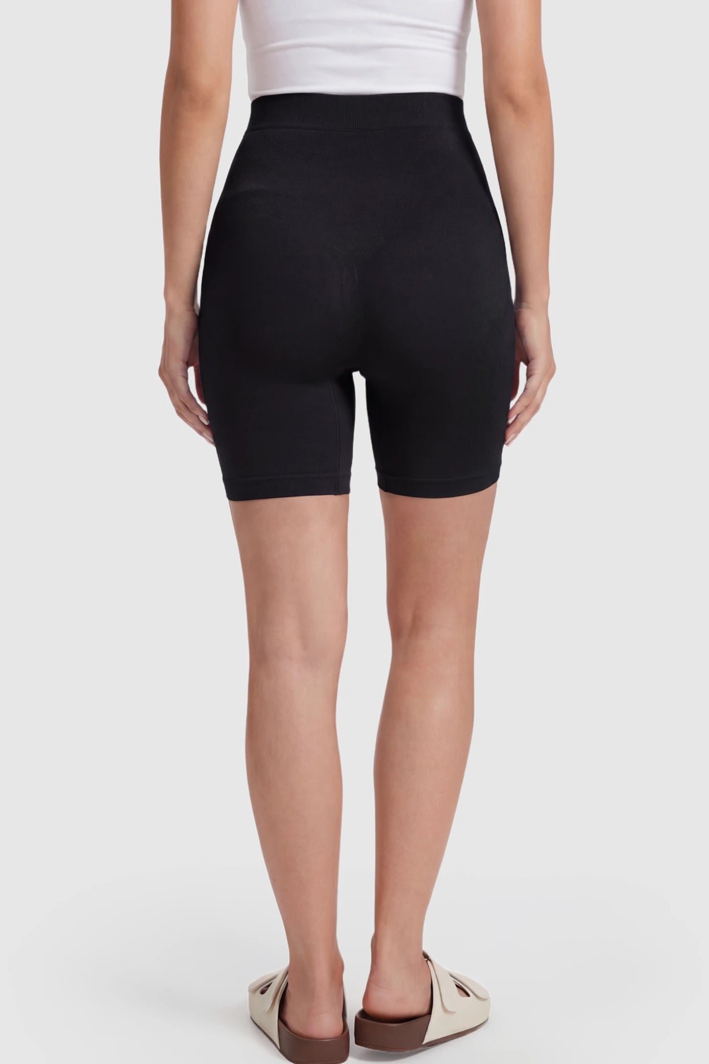 Seamless High Waisted Maternity Shapewear Shorts Seamless High-Waisted Mid Thigh Maternity Shapewear Shorts in Black featuring a smooth belly support panel on a pregnant model showing back.